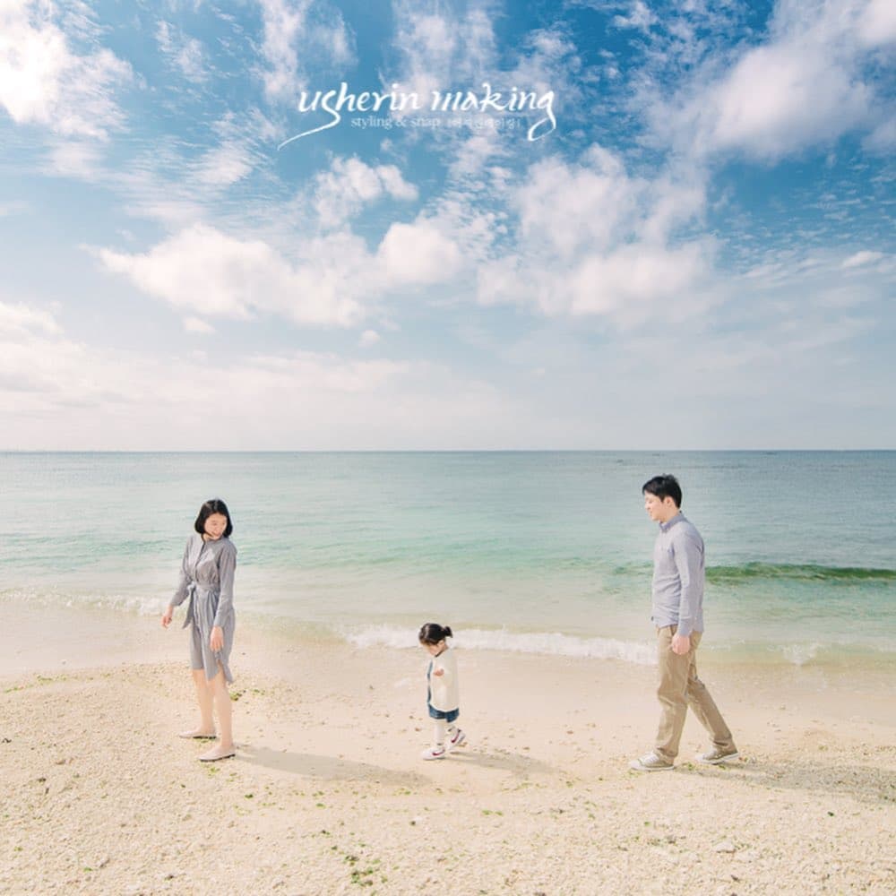 A family of three strolls along a bright Okinawa beach under a wide blue sky