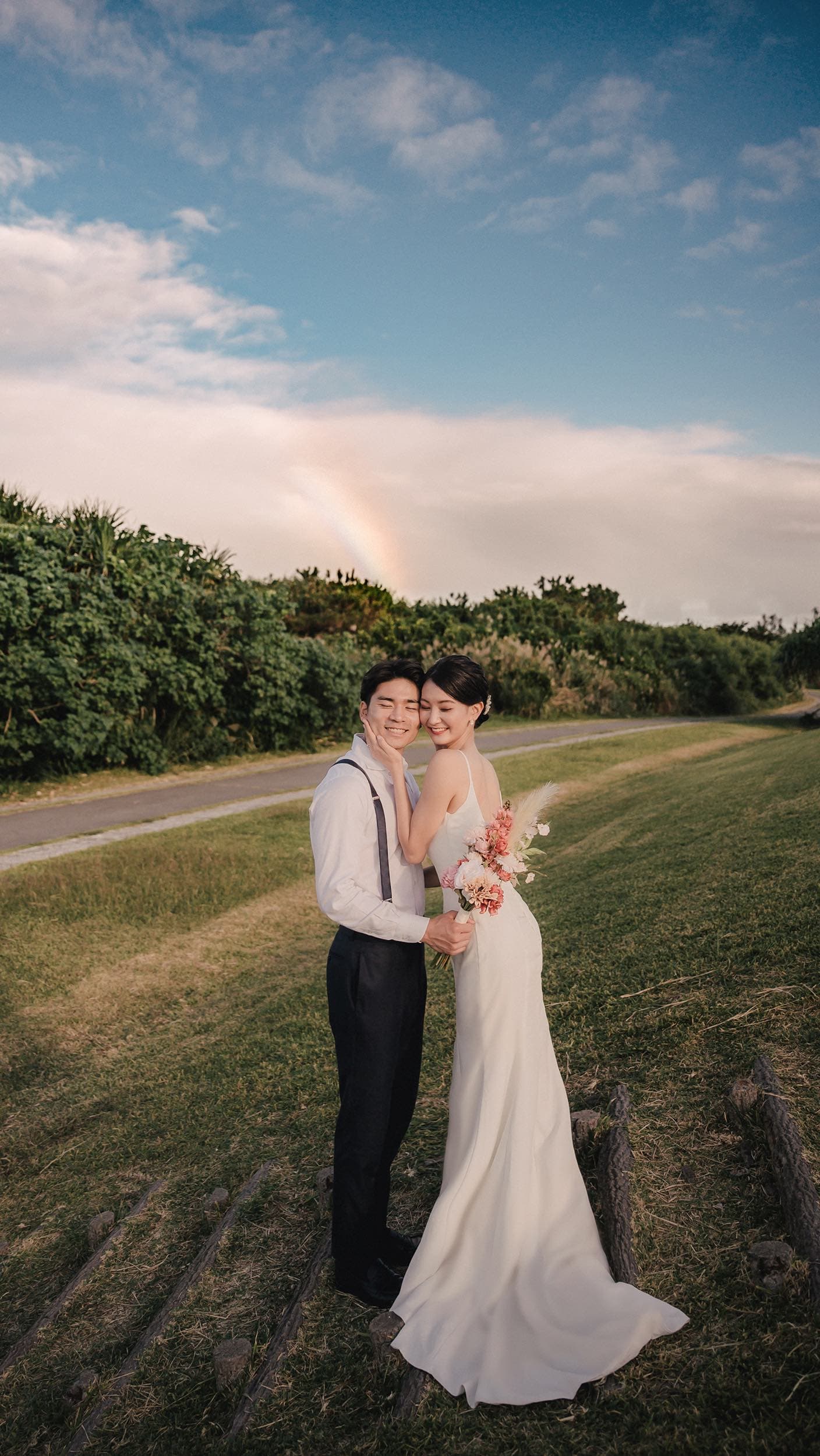 Bride and groom cheek to cheek under a faint rainbow in Okinawa