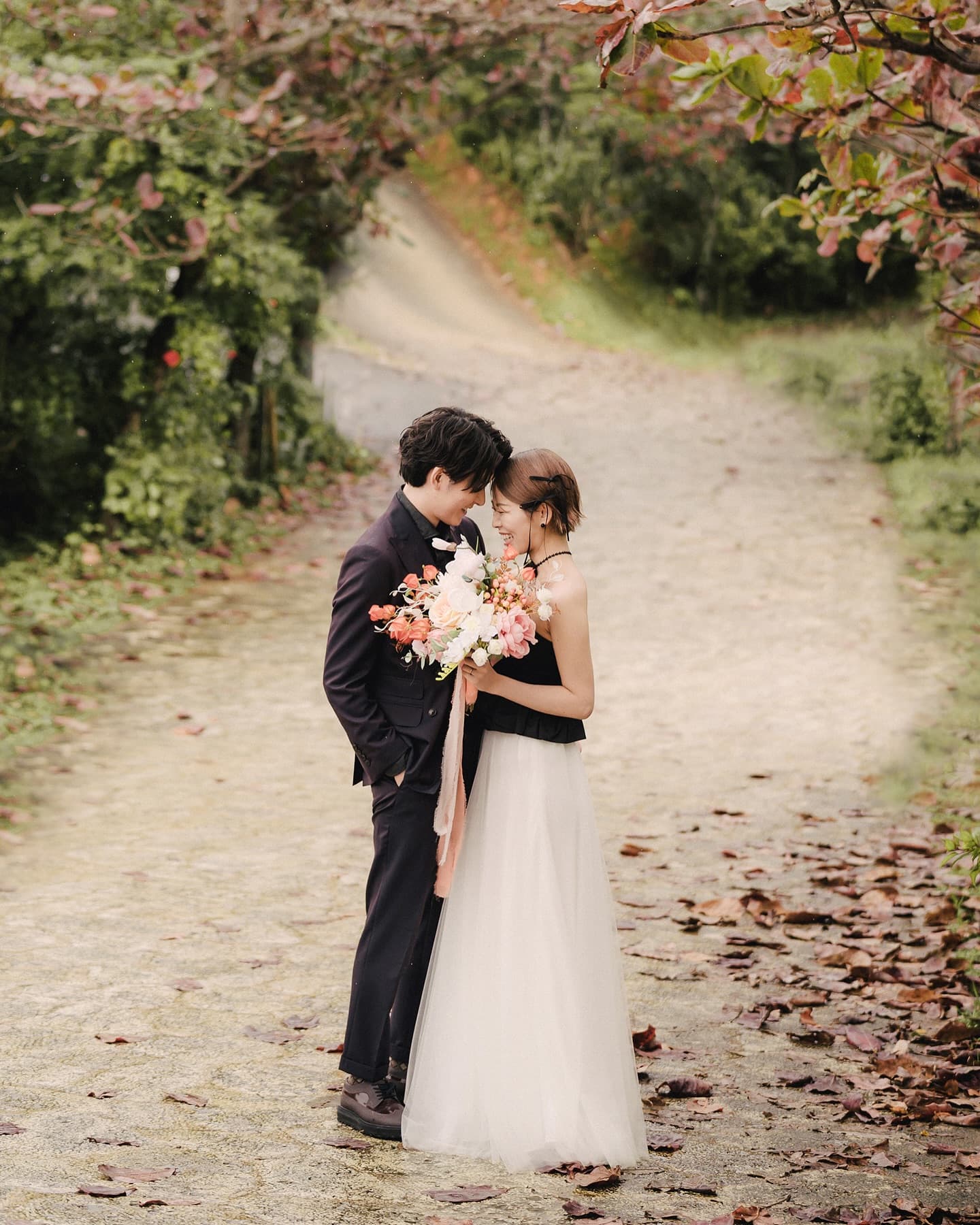 Couple touching foreheads over a bouquet on a leafy path, Okinawa