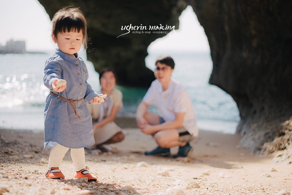 沖縄の浜辺で貝殻を見せる女の子と見守る両親