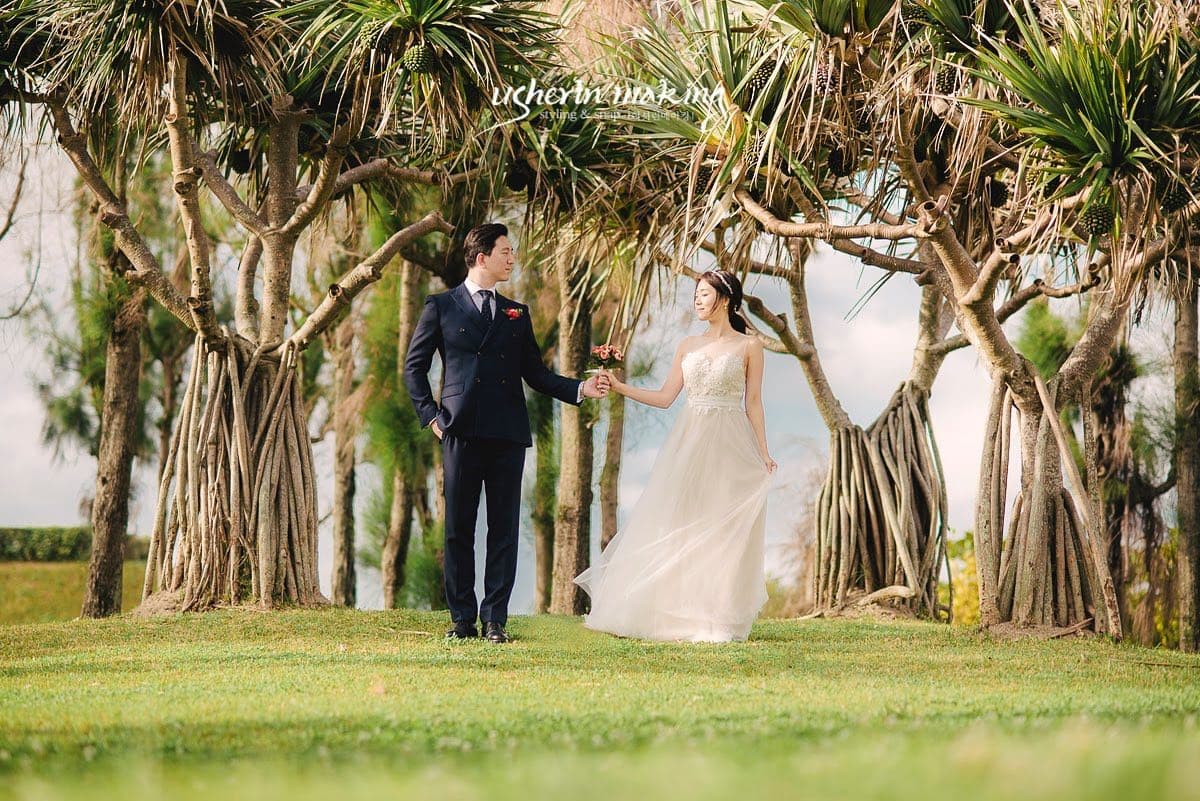 アダンの木が並ぶ芝生で手を取り合って歩く新郎新婦