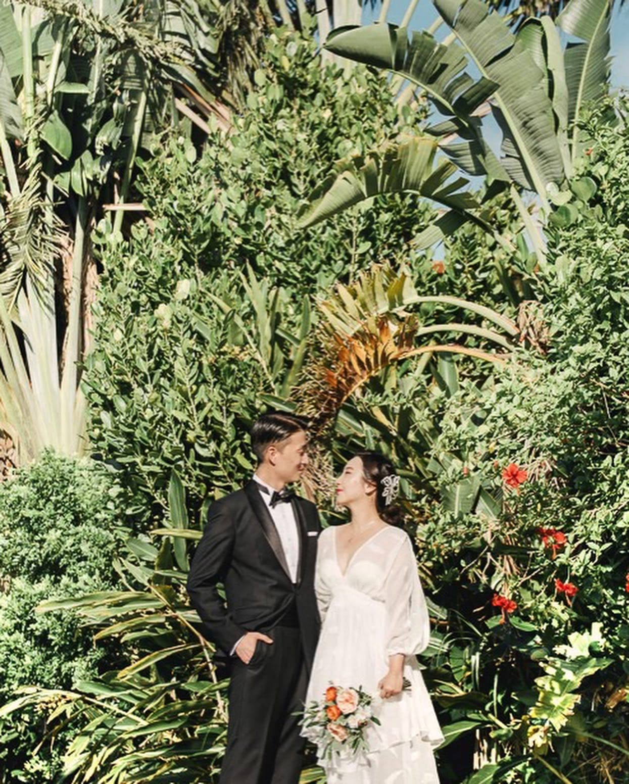 Bride and groom smiling amid tropical foliage and red hibiscus in Okinawa