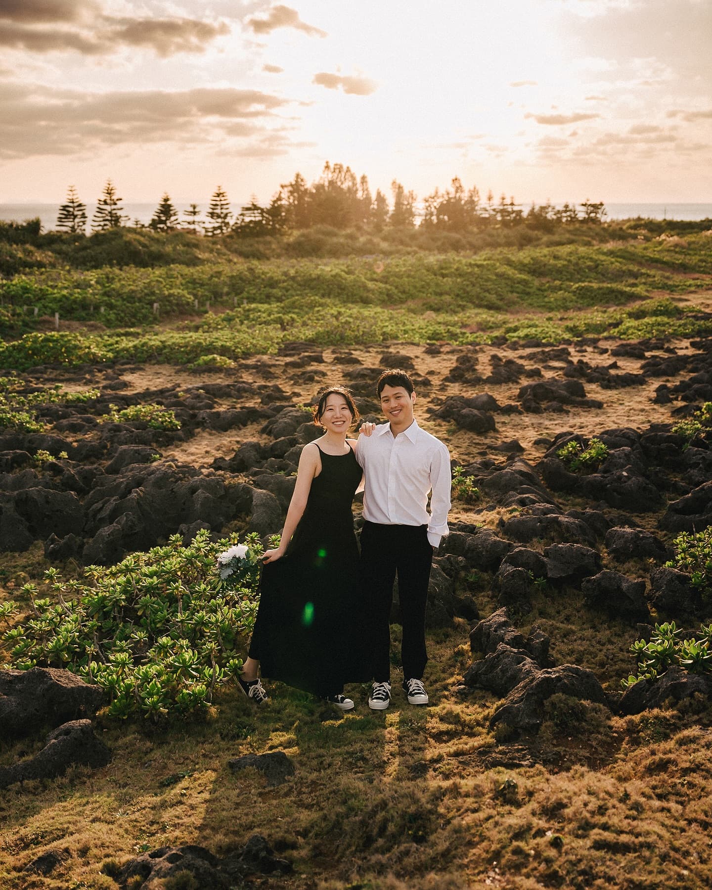 Couple standing side by side in a sunset-lit rocky meadow by the sea in Okinawa