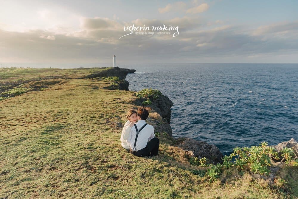 Couple sitting together on a grassy Okinawa cape with a lighthouse in the distance