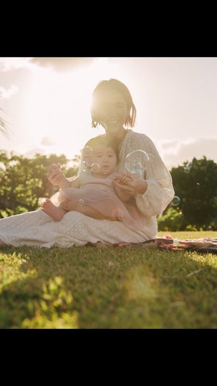 Mother sitting on the grass holding her baby among soap bubbles in warm backlight