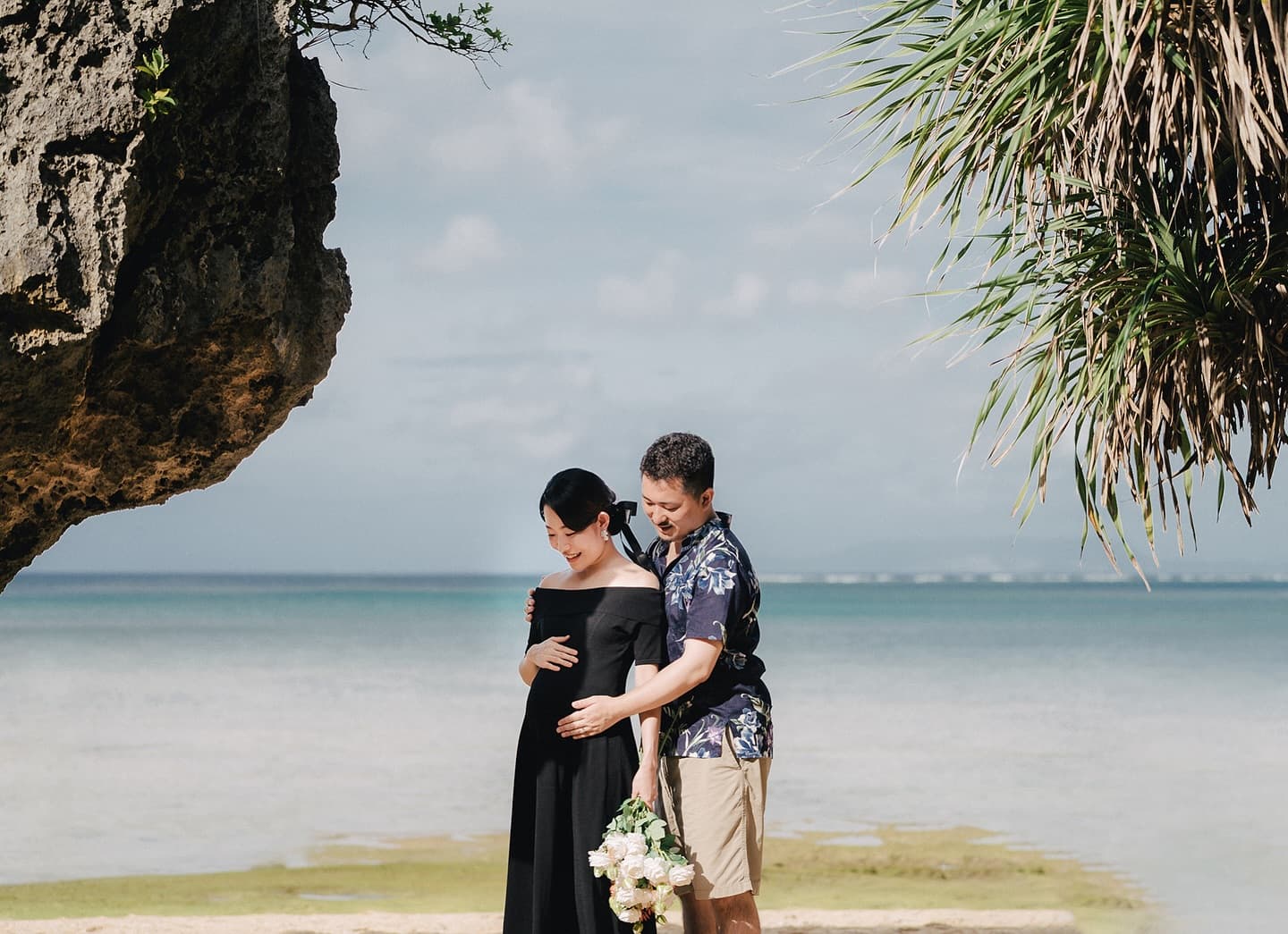 Husband gently embraces his pregnant wife on an Okinawa beach
