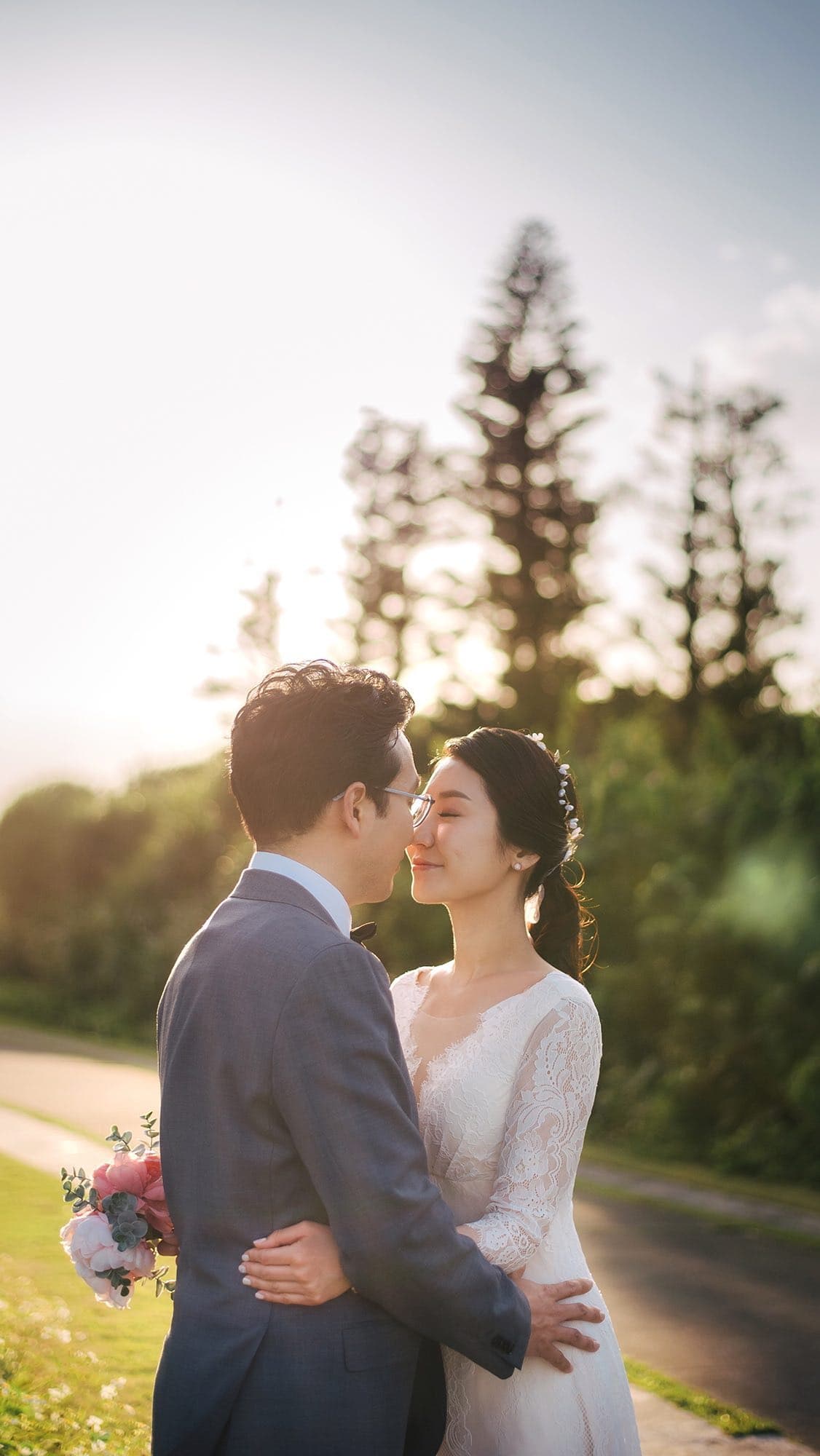 황금빛 역광이 비치는 오키나와 녹음 속에서 이마를 맞댄 신랑 신부