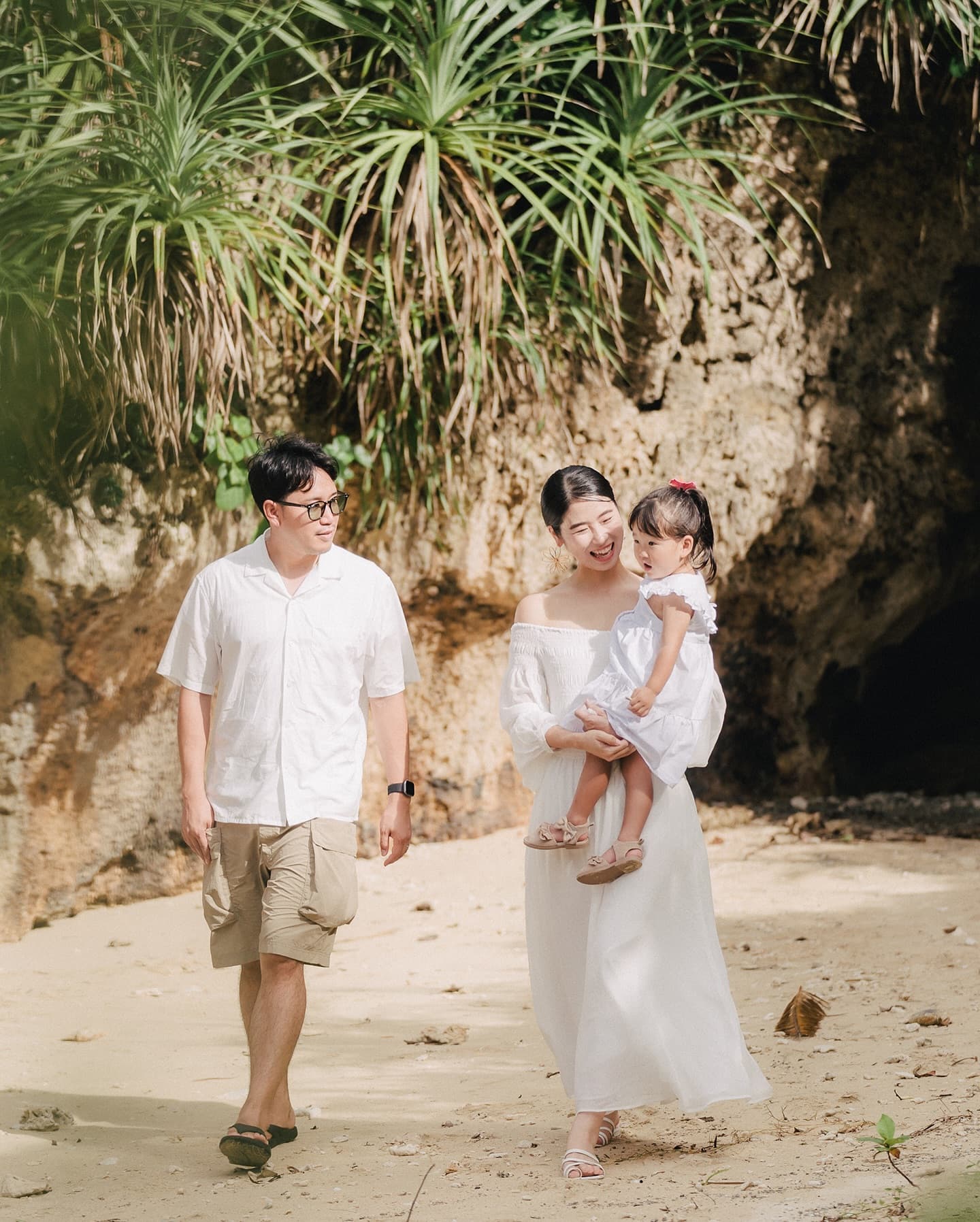 Family of three strolling on the sand beneath palms in Okinawa