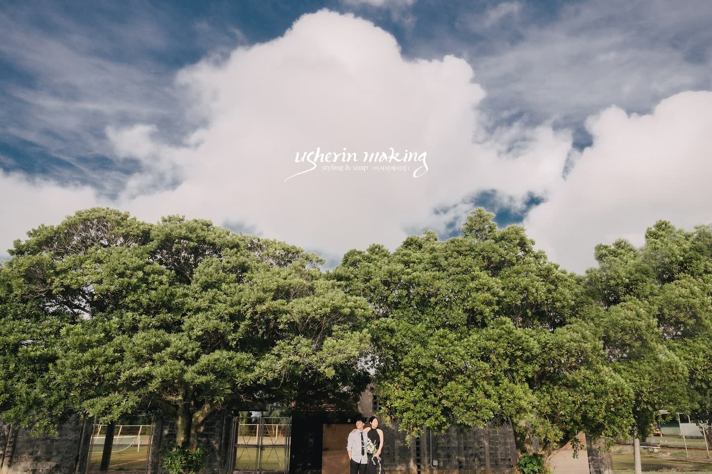 Couple standing small beneath towering clouds and lush green trees on Miyako Island, Okinawa