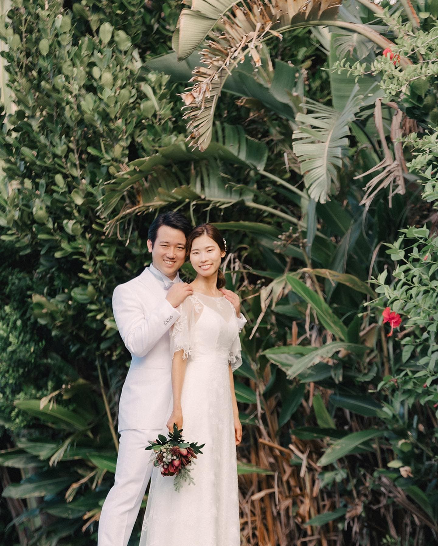 Bride and groom in white smiling before lush tropical greenery in Okinawa