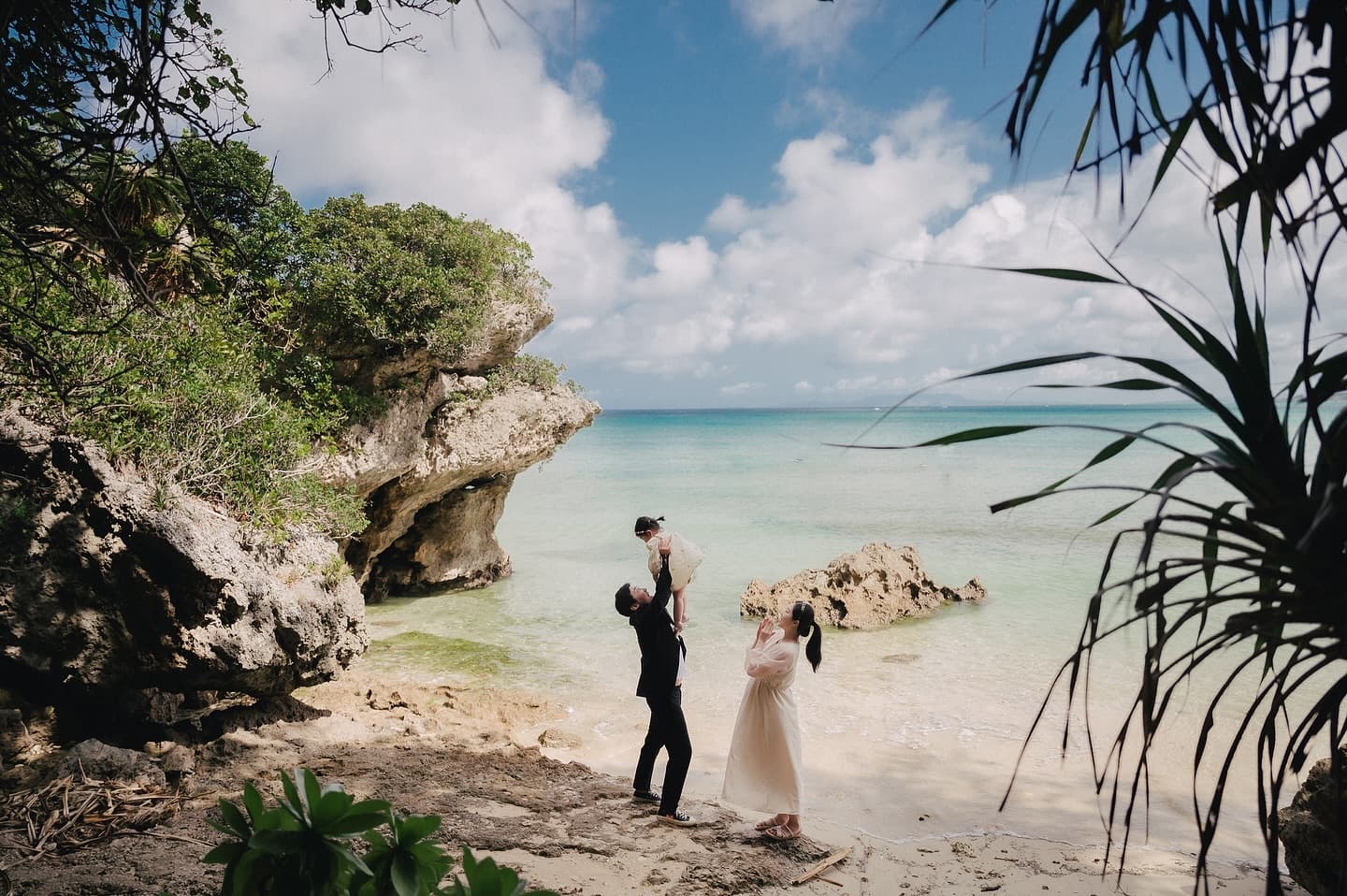 Father lifting his child in a rocky Okinawa cove while the expecting mother looks on