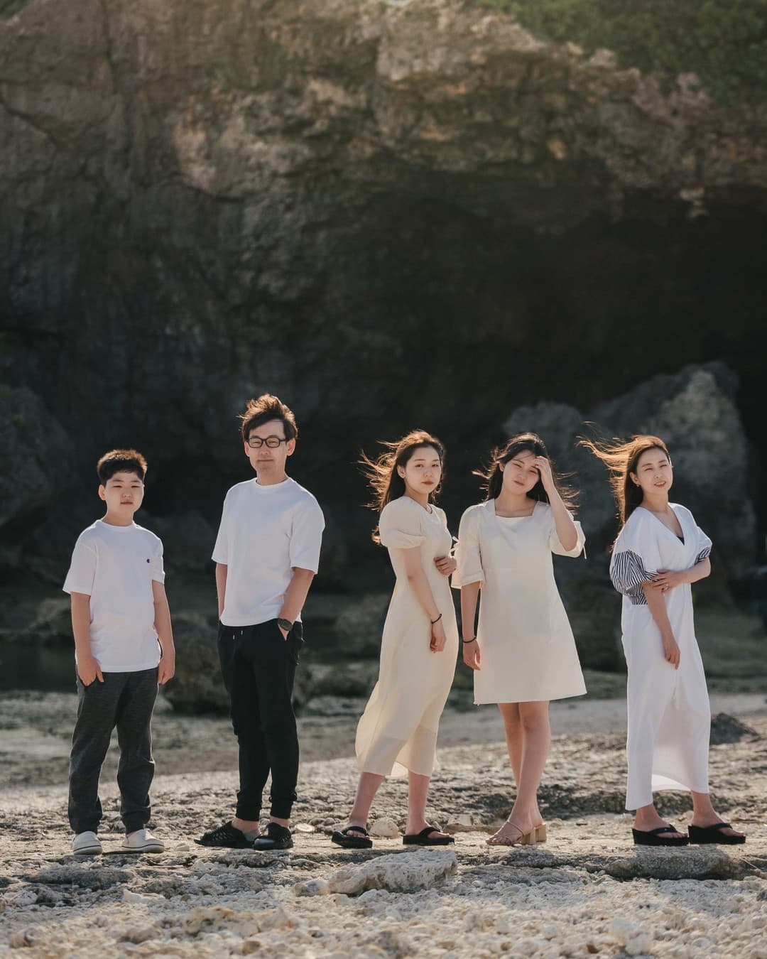 Family of five standing in a row on a rocky Okinawa beach in white outfits