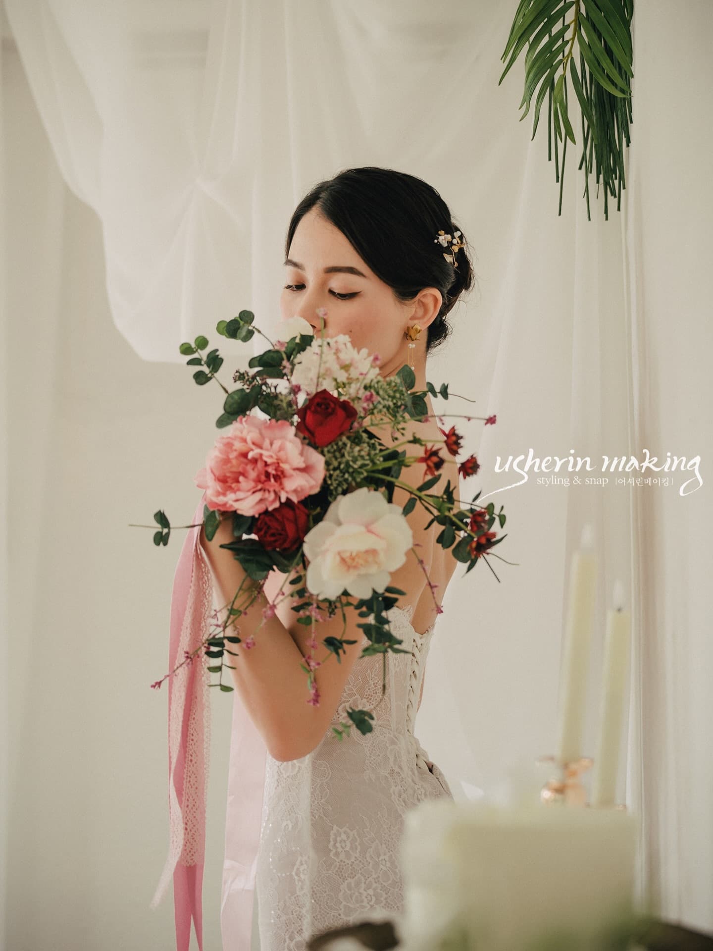 A bride holds a pink and red bouquet close to her face in the studio