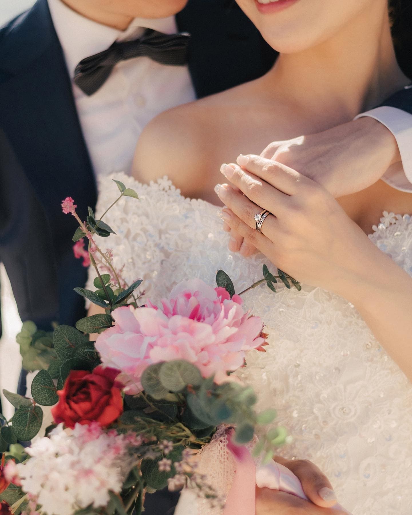 Close-up of a bride's hand with her wedding ring resting over a pink bouquet