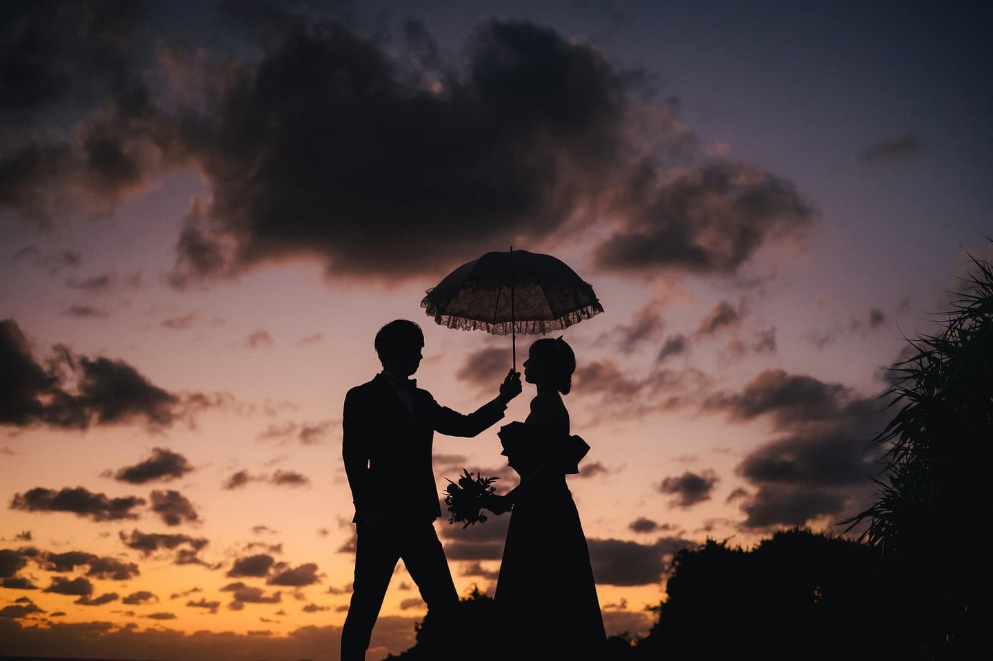 茜色の夕焼け空にレースの日傘を差し向き合うカップルのシルエット、沖縄