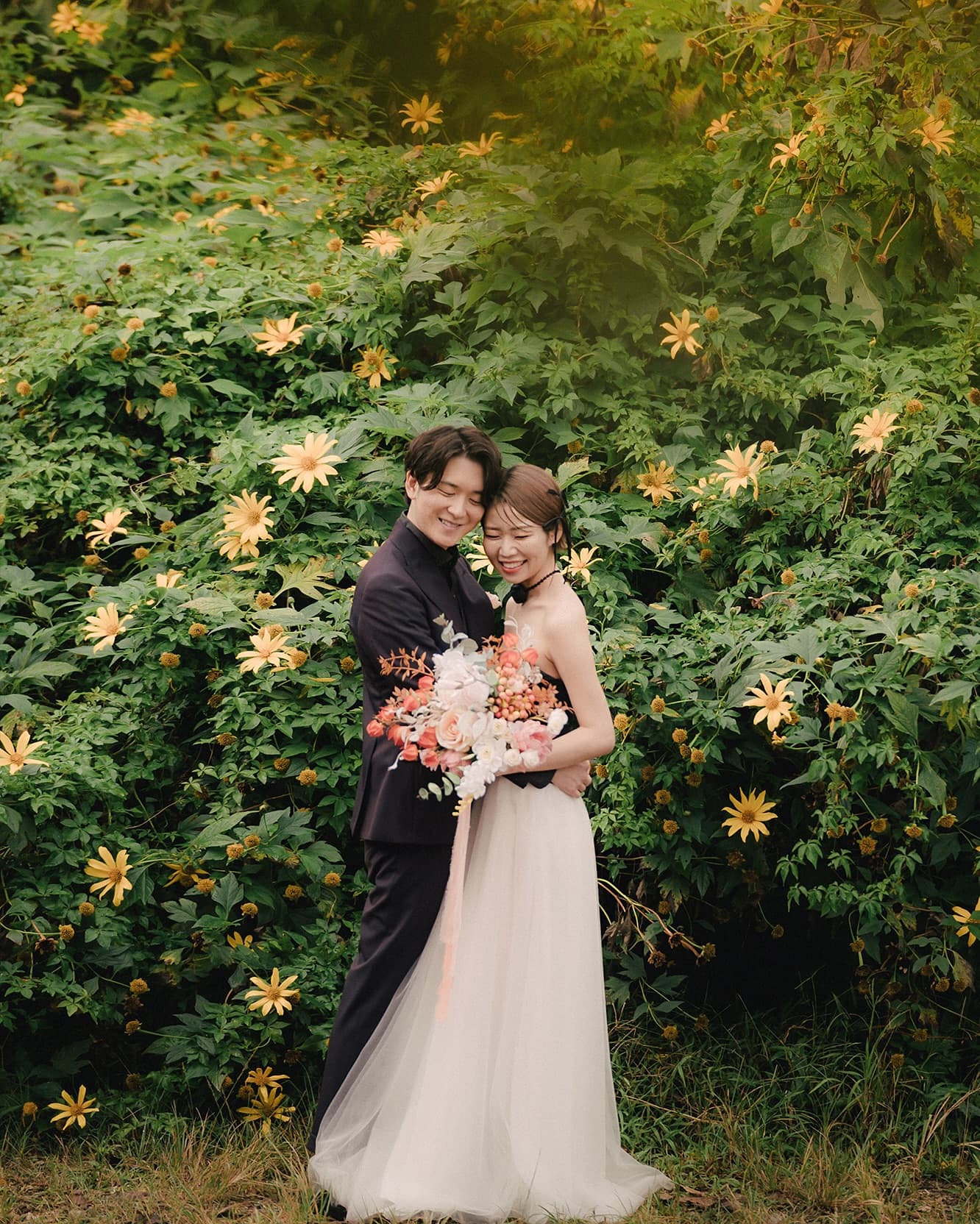 黄色い花が咲く緑の茂みの前で抱き合う新郎新婦、沖縄