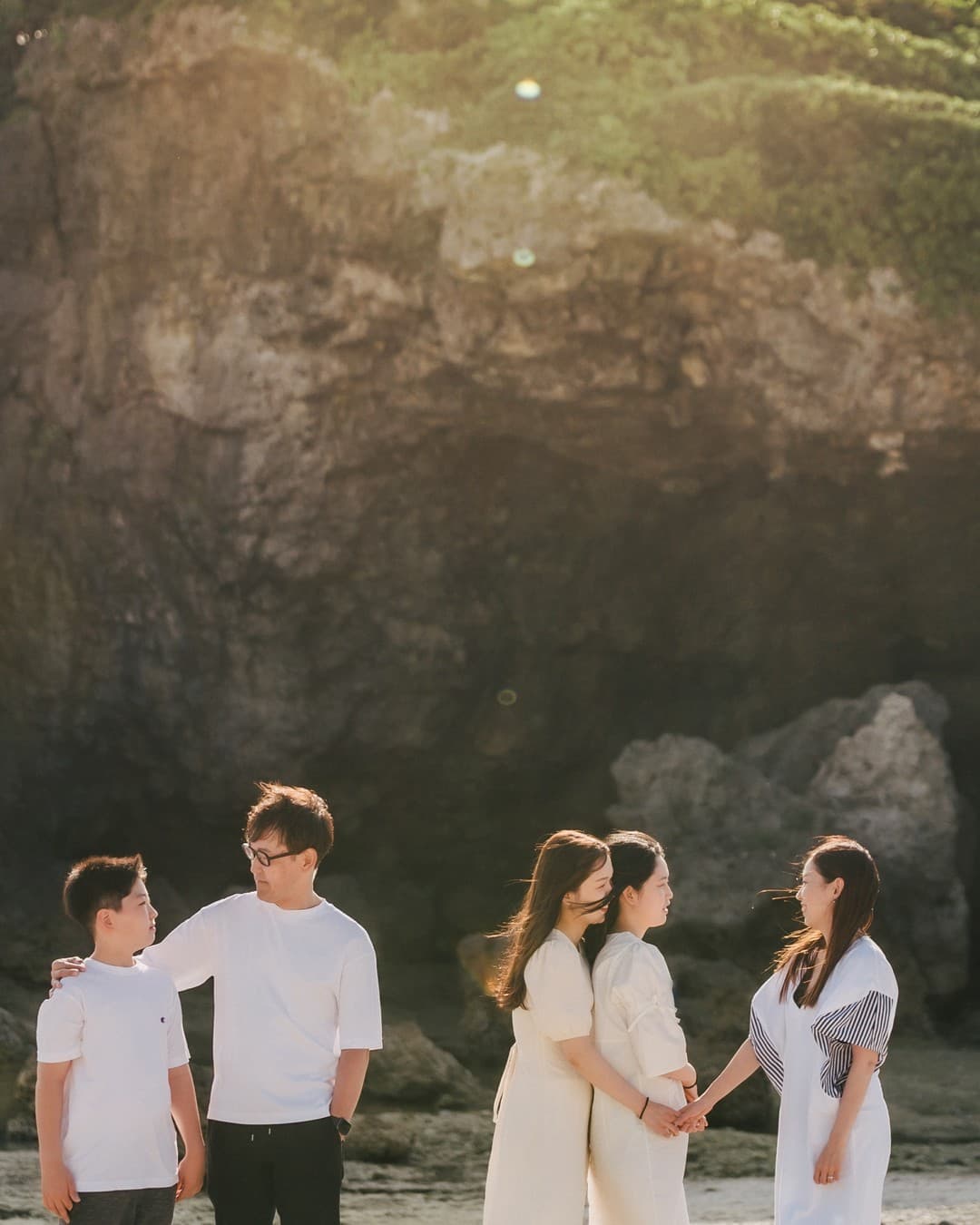 Family of five in white gathered before a rocky cliff on an Okinawa beach