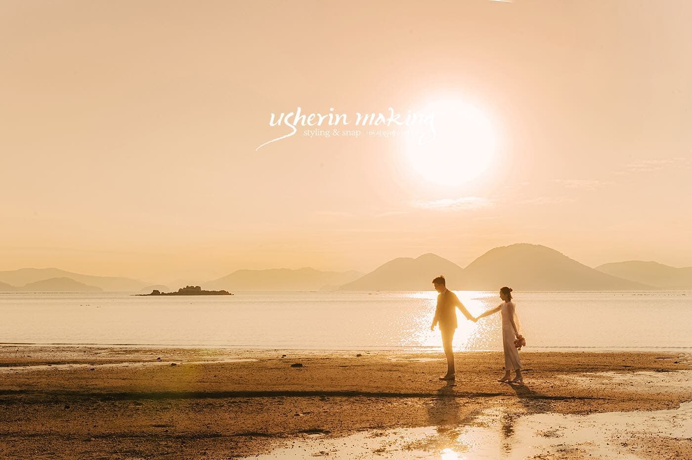大きな夕日と島影を望む浜辺を手をつないで歩く二人