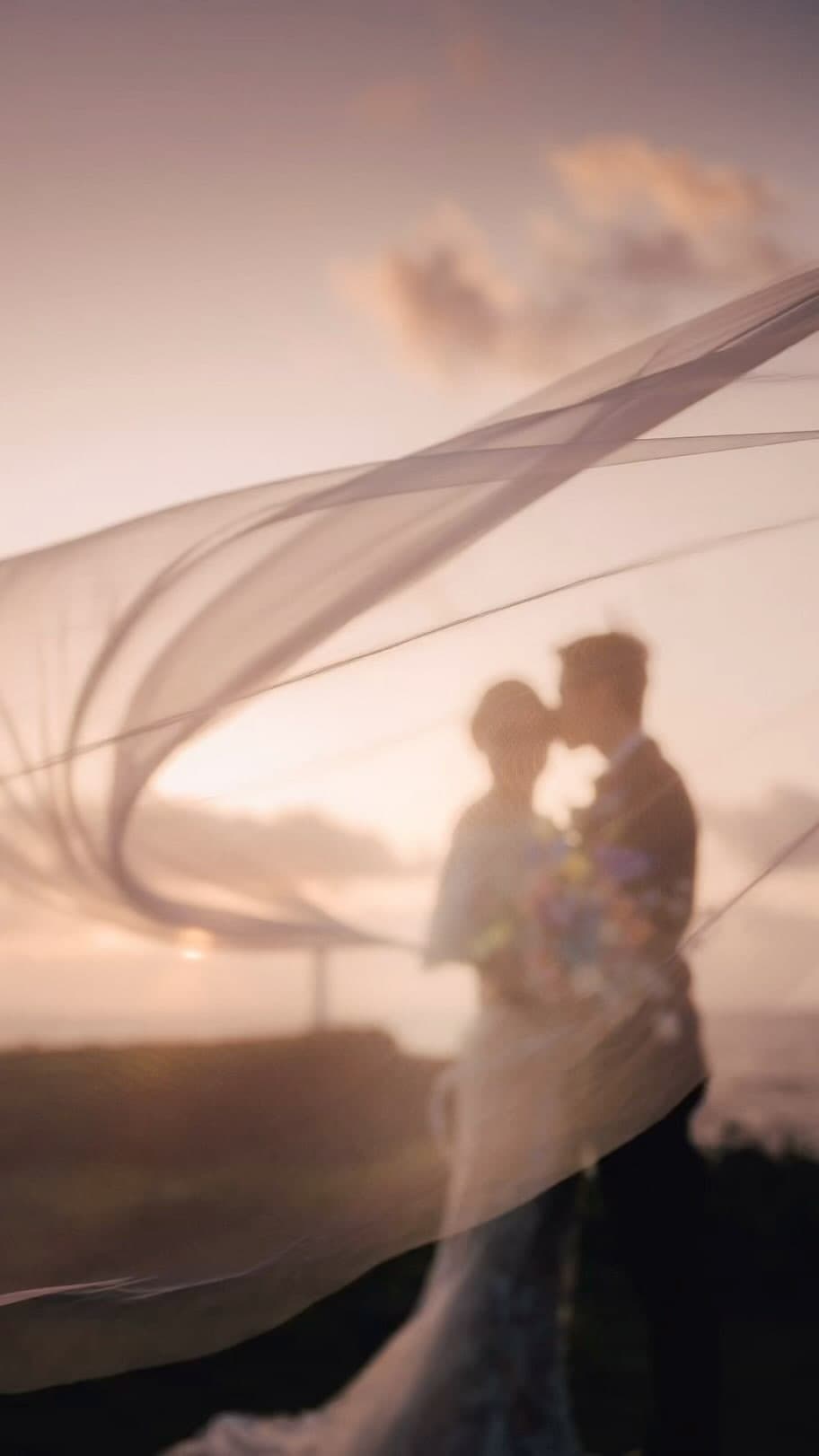 Long veil sweeps a sunset sky as the couple embraces in Okinawa