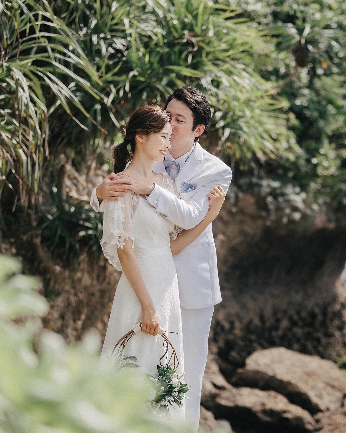 Groom kissing his bride's forehead by pandanus greenery on the Okinawa coast