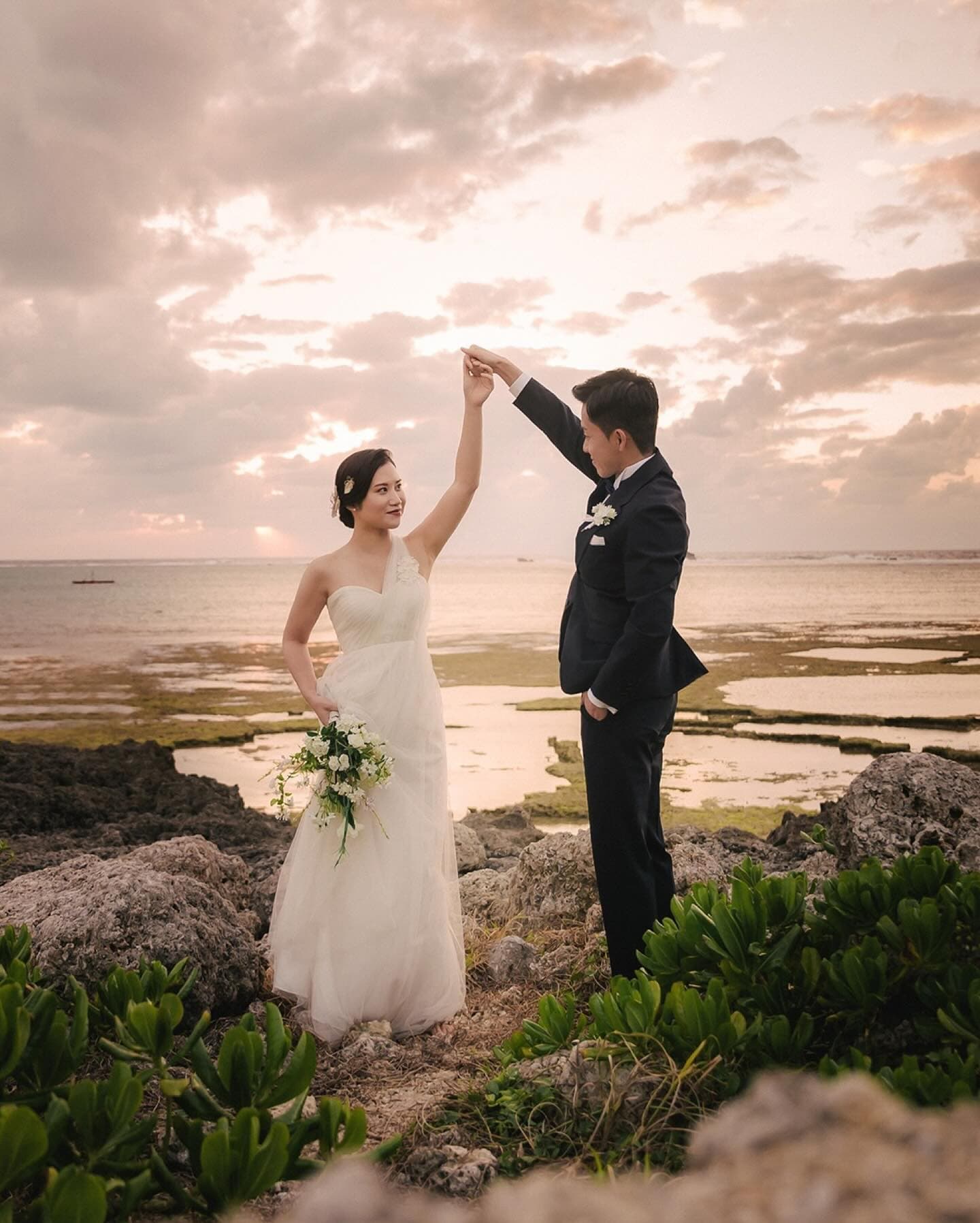 Groom twirling the bride on a rocky shore at sunset in Okinawa