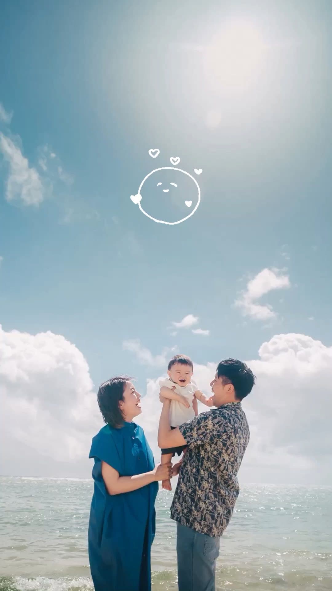 Parents lifting their baby high on an Okinawa beach under a bright blue sky