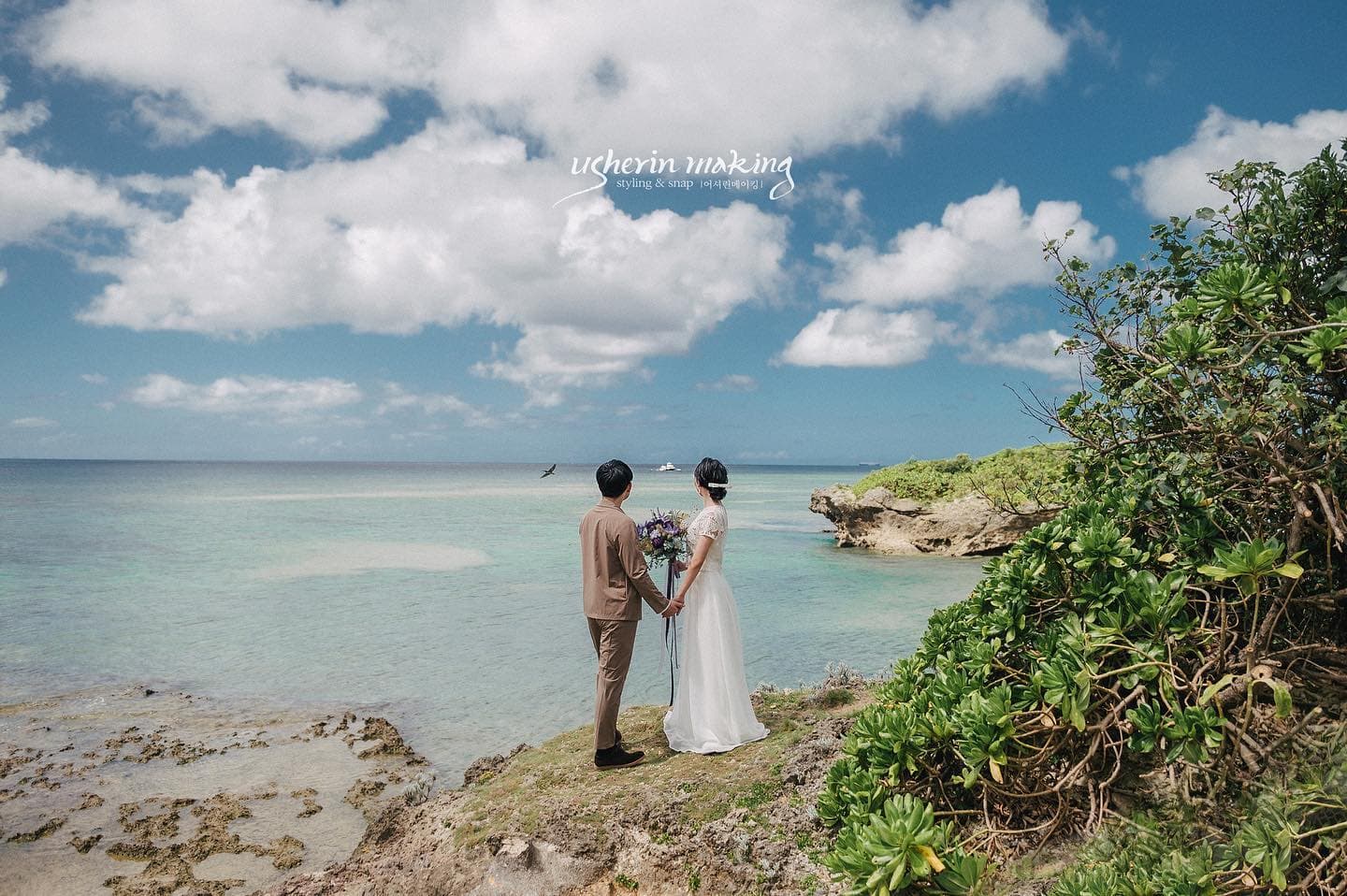 Bride and groom holding hands on a headland above Okinawa's emerald sea