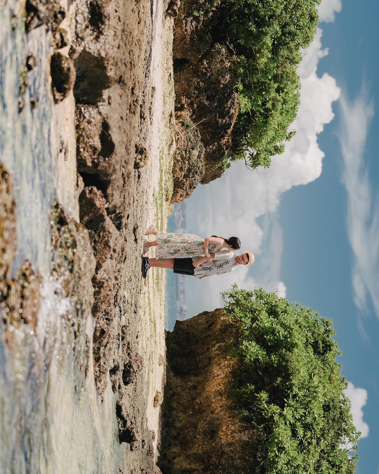 Couple standing on a rocky Okinawa shore under a clearing blue sky