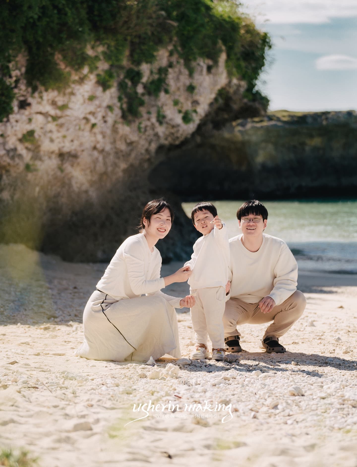 Family of three crouching together on a white-sand beach on a clear day in Okinawa