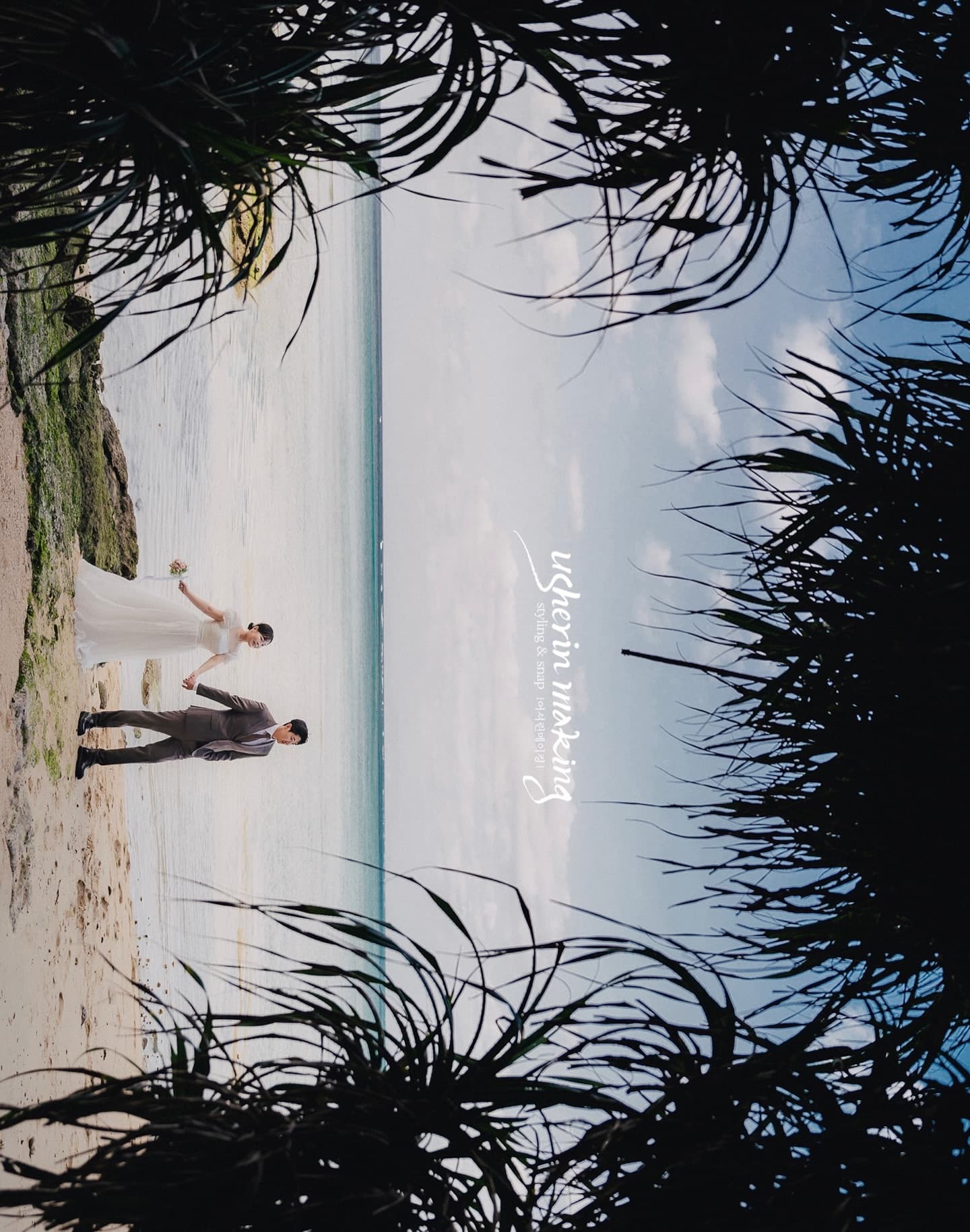 Bride and groom on a white beach framed by dark adan leaves in Okinawa