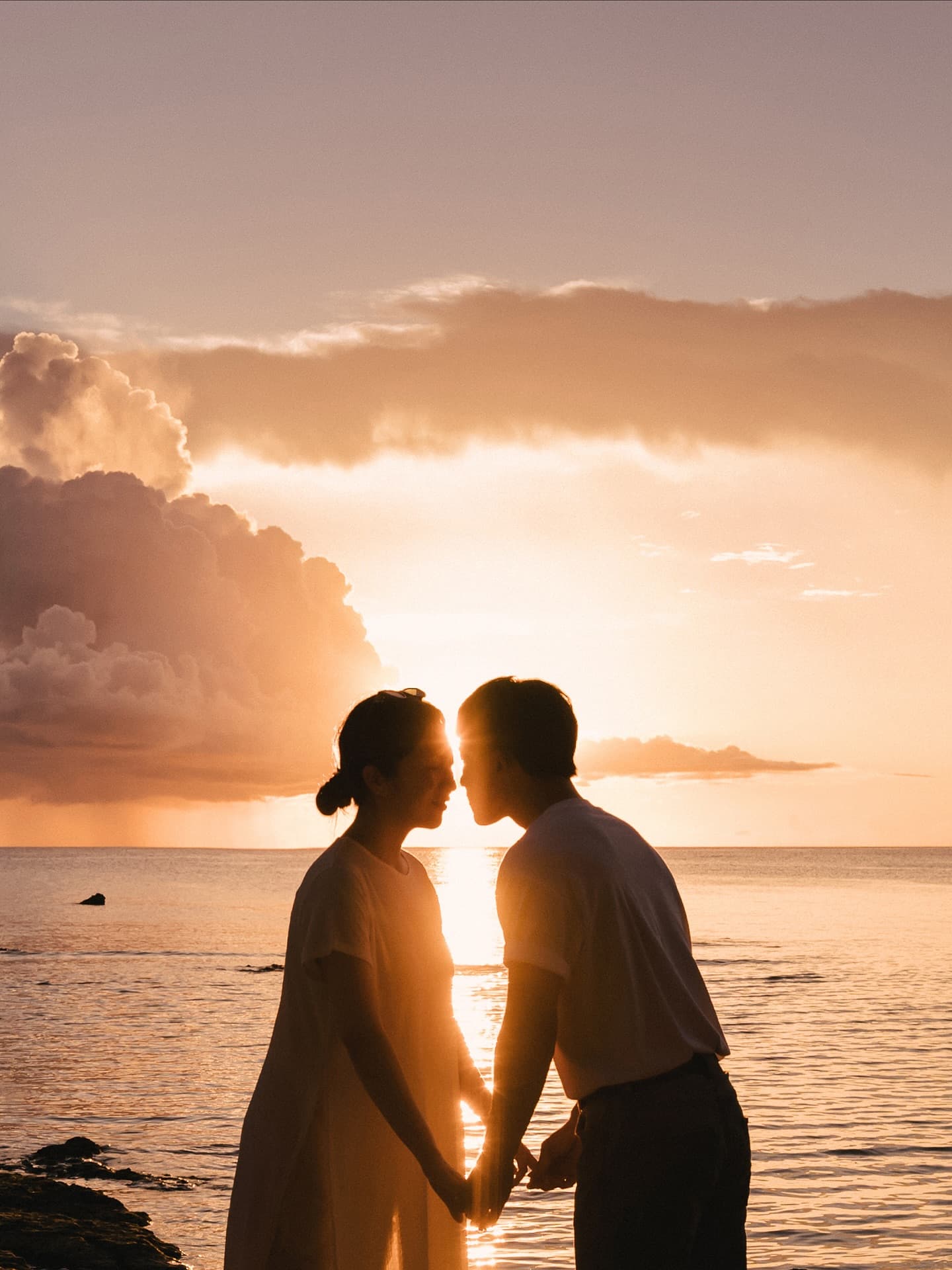 Couple silhouetted nose to nose against a golden Okinawa sunset sea