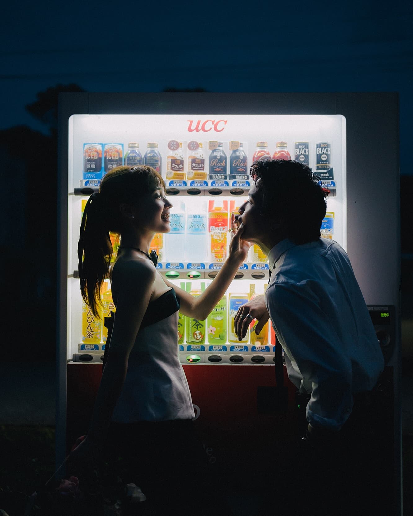 Bride playfully touching the groom chin by a night vending machine