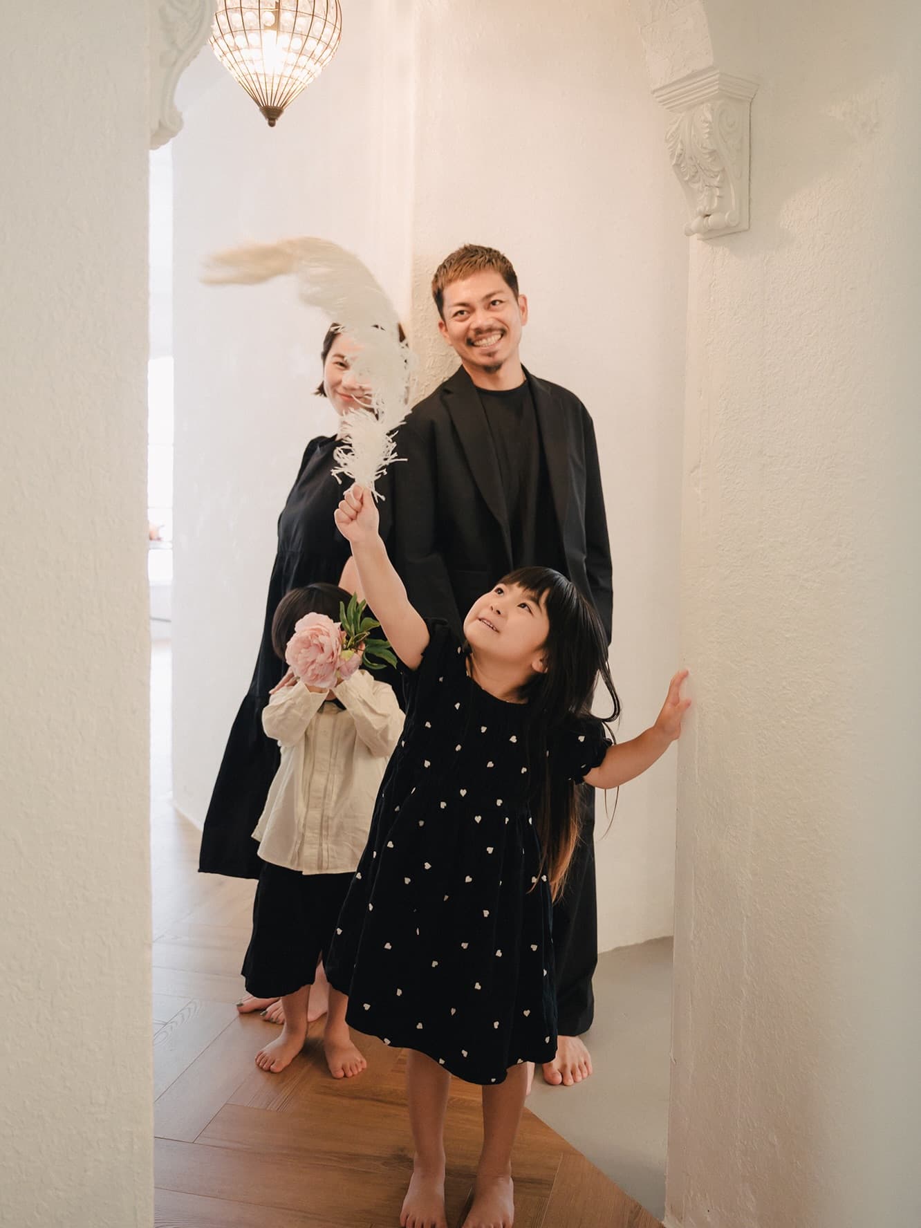 Family portrait in a white studio hallway, the children playing with flowers