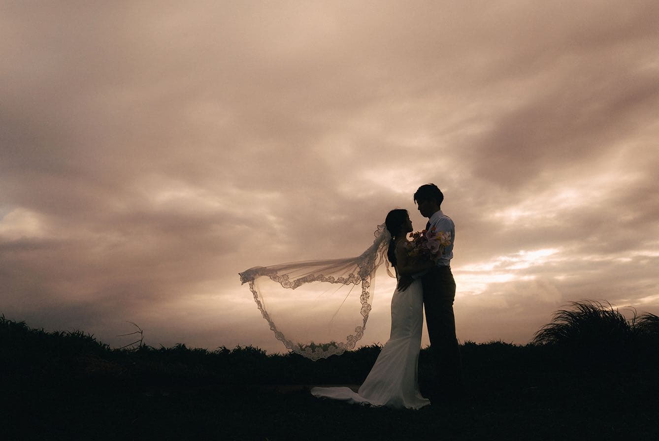 Couple embracing in silhouette as the bride's veil drifts in the sunset wind