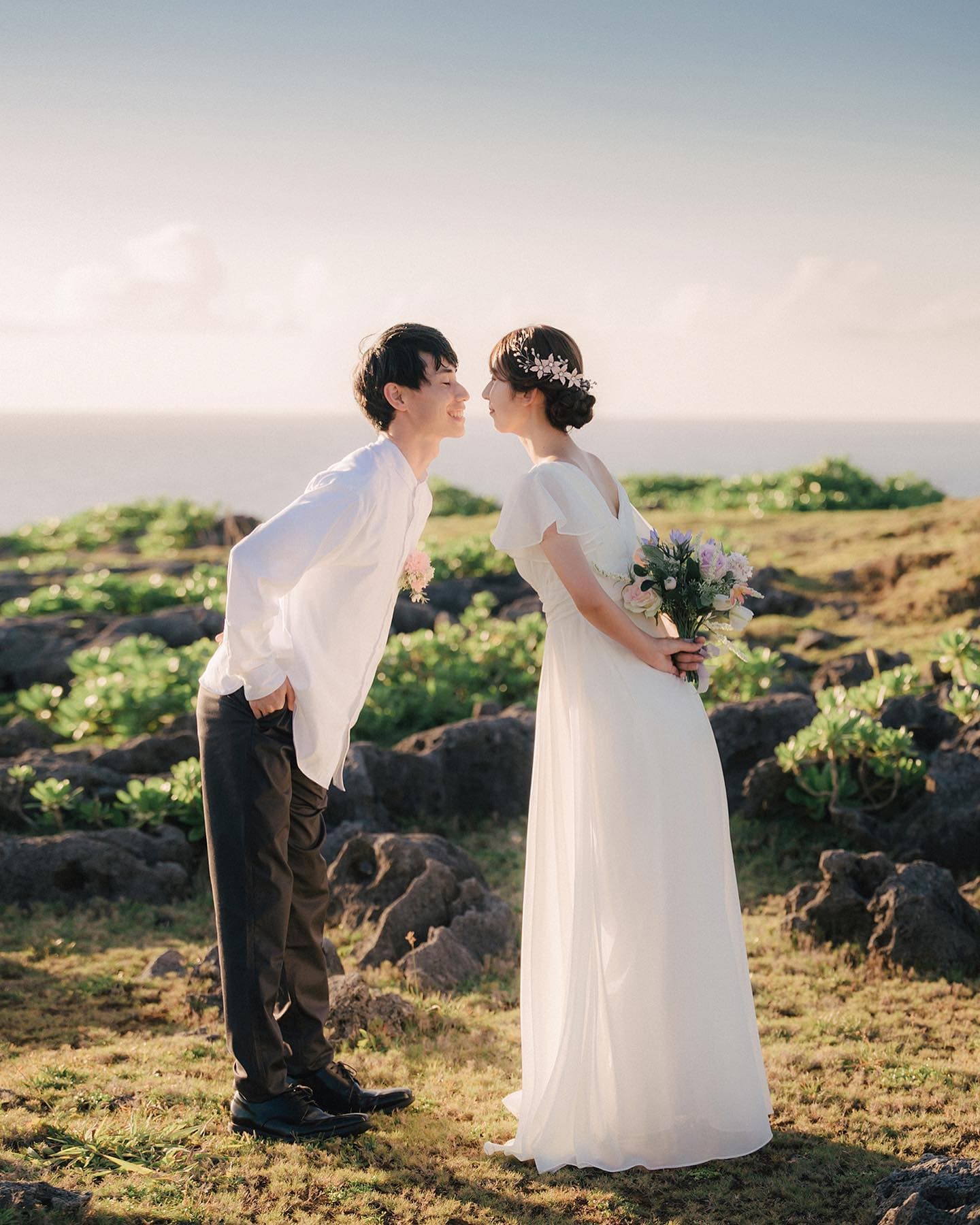 Couple leaning in for a kiss on a rocky seaside meadow in Okinawa