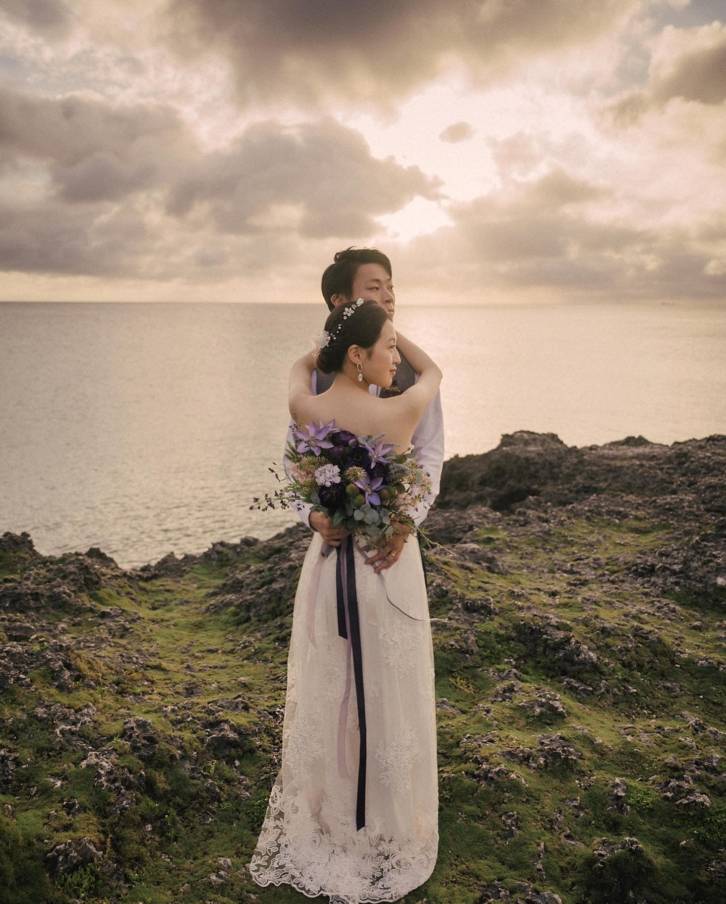 Groom holding his bride on an Okinawa cliff as light breaks through the clouds