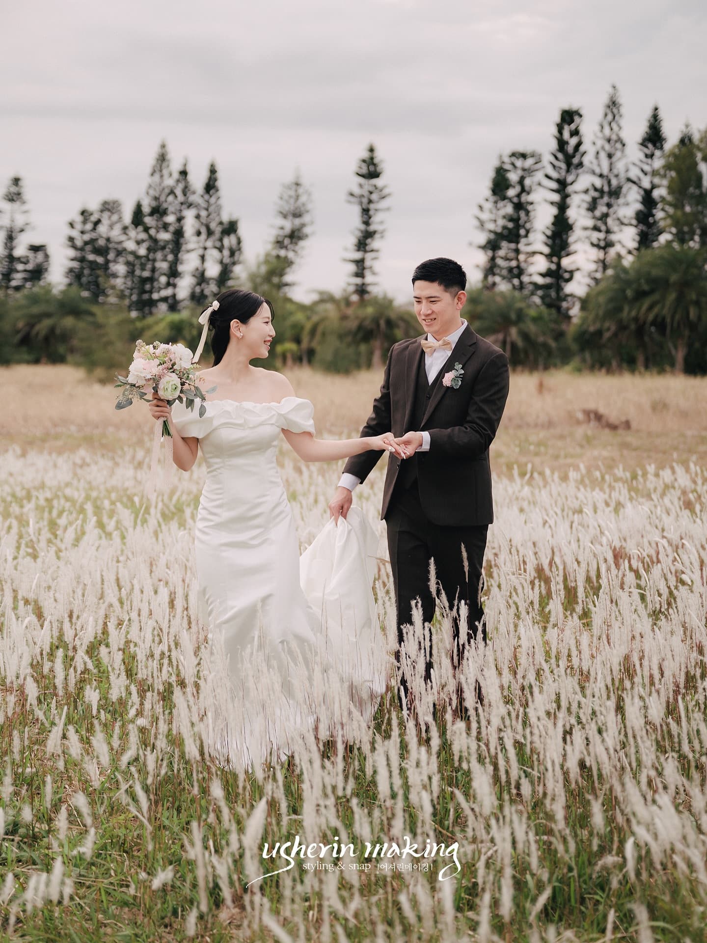 Groom leading his bride by the hand through a field of silvery grass in Okinawa