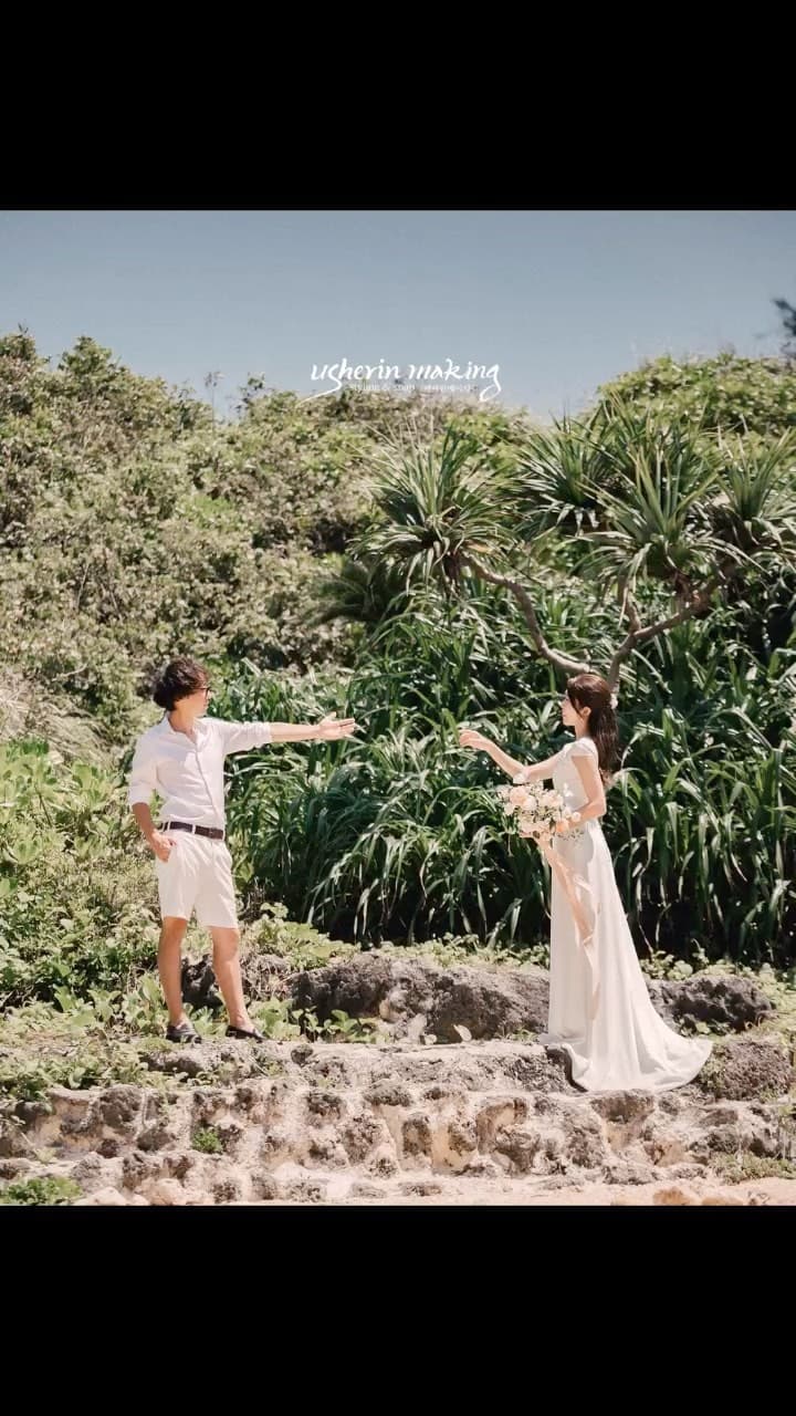 Couple in white reaching toward each other among lush tropical greenery in Okinawa