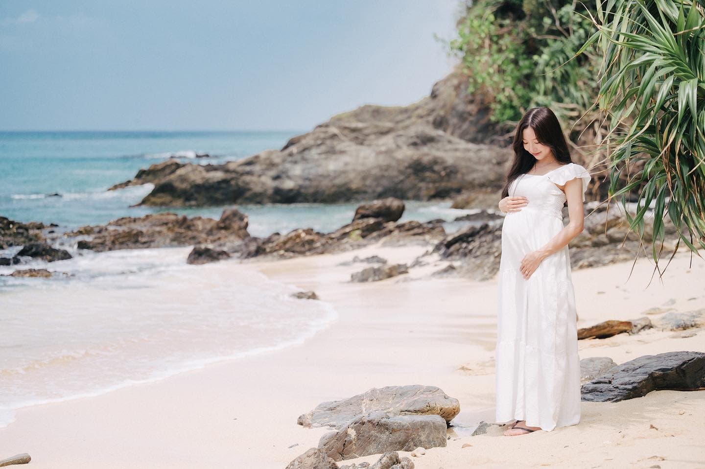 Expectant mother in white cradling her belly on an Okinawa beach