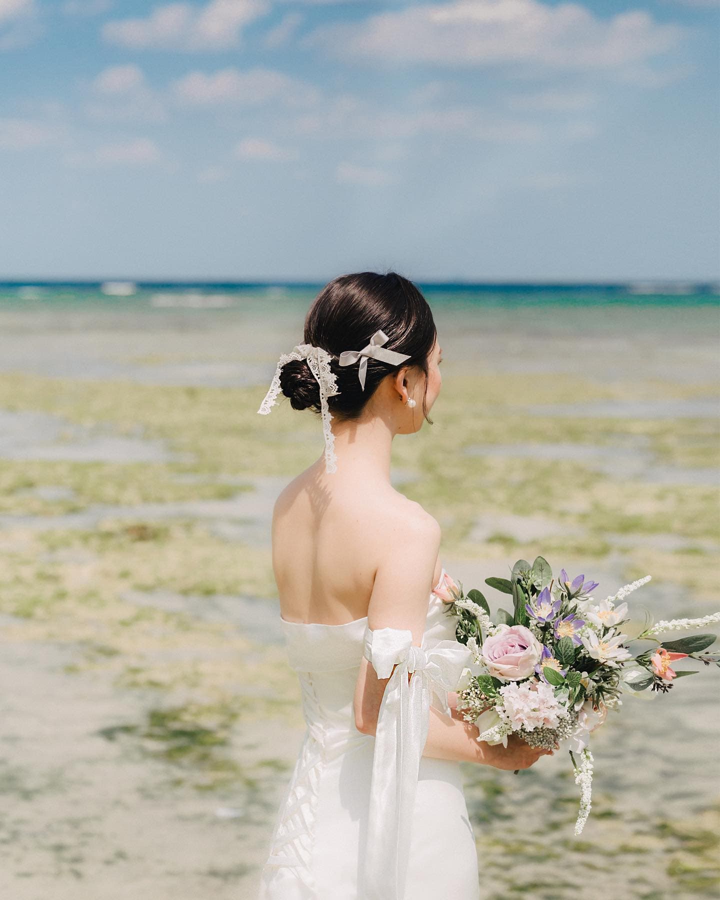 Bride seen from behind holding her bouquet before the blue Okinawa sea