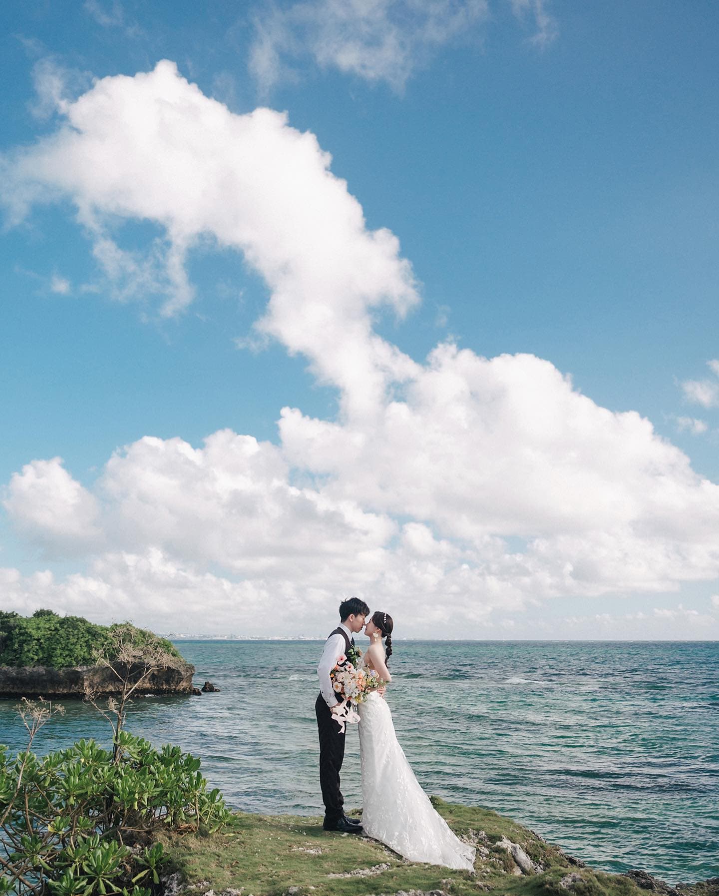 Couple sharing a kiss on a seaside cliff under billowing clouds in Okinawa