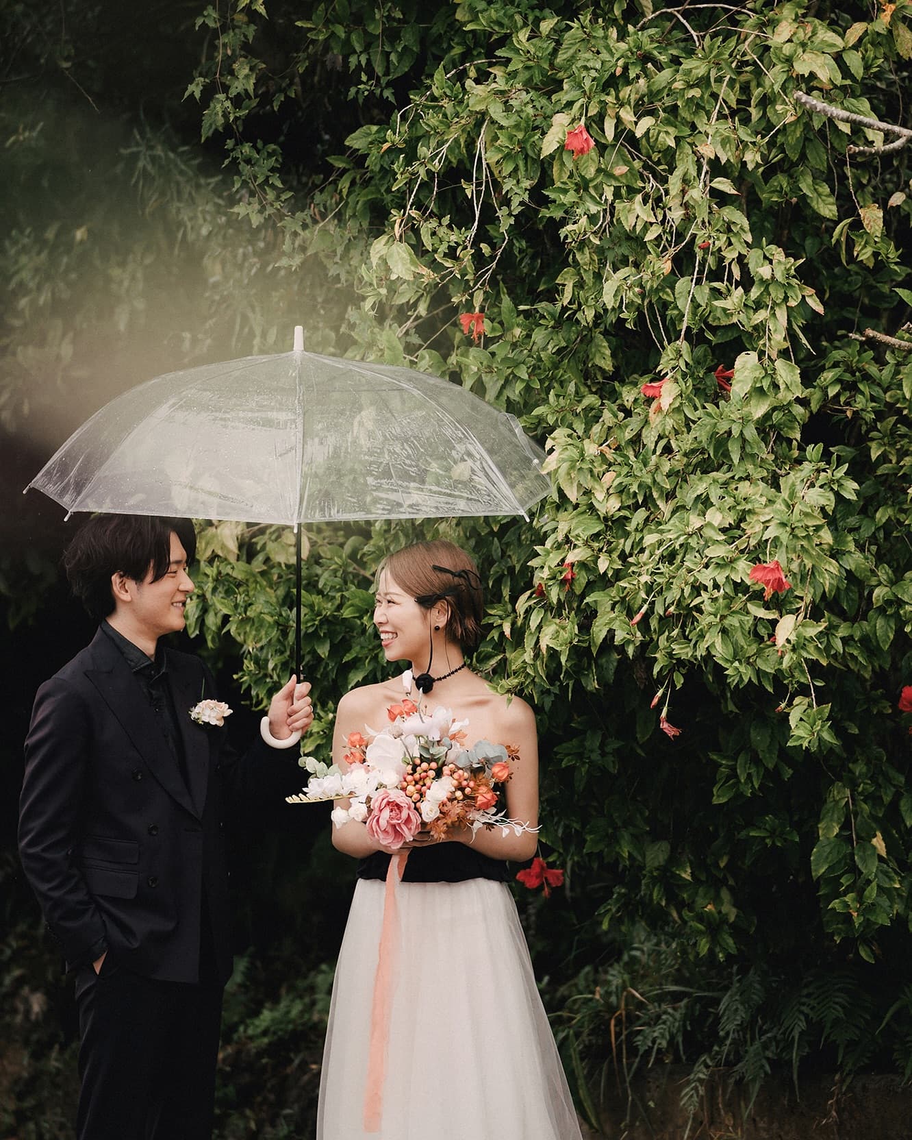 Couple under a clear umbrella by red hibiscus on a rainy Okinawa day