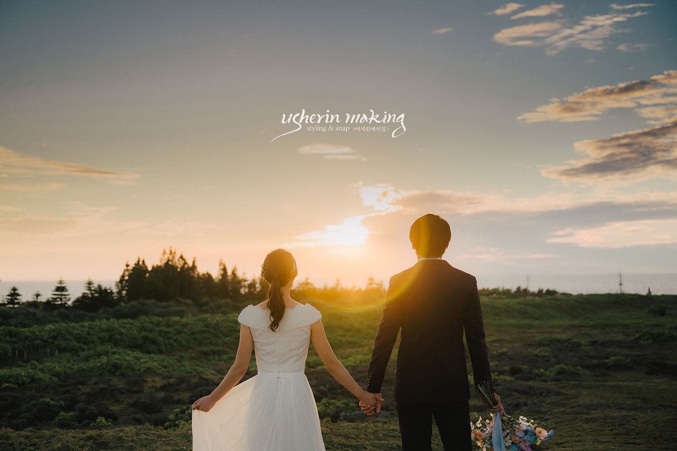 Bride and groom walking hand in hand toward the setting sun across a grassy field