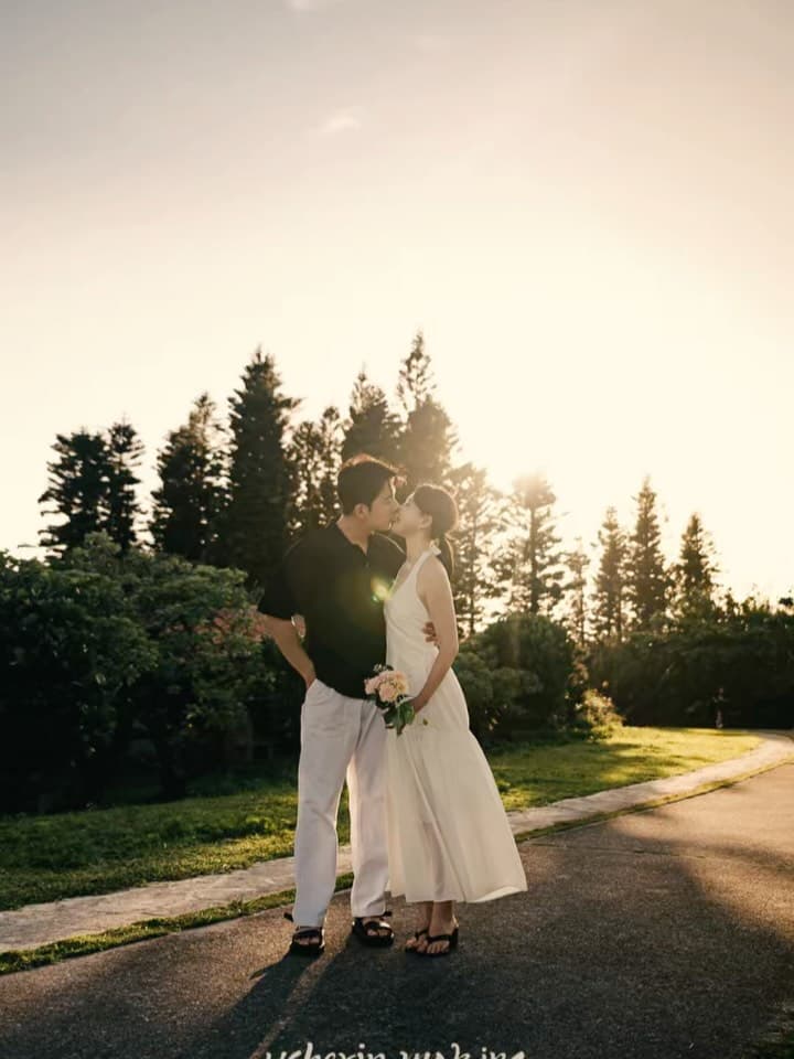 夕日を背にキスを交わす新郎新婦、松の木立が並ぶ沖縄の夕暮れ