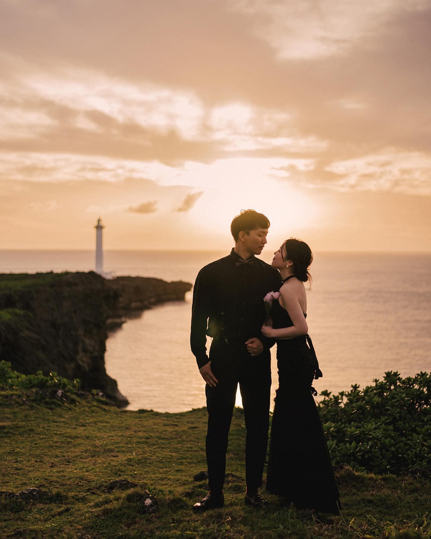 Couple in black embracing on a sunset cape by an Okinawa lighthouse