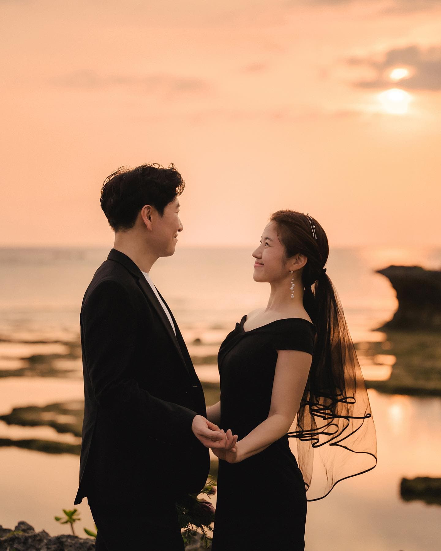Couple in black holding hands on a sunset shore, Okinawa