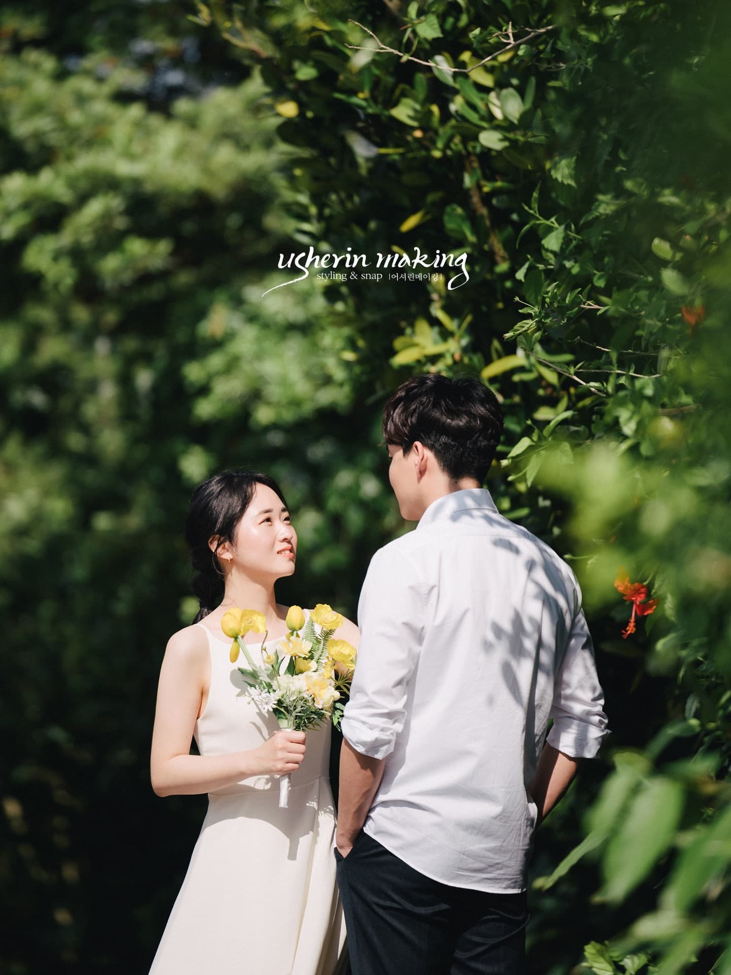 Bride with a yellow bouquet smiling at the groom amid lush greenery in sunny Okinawa