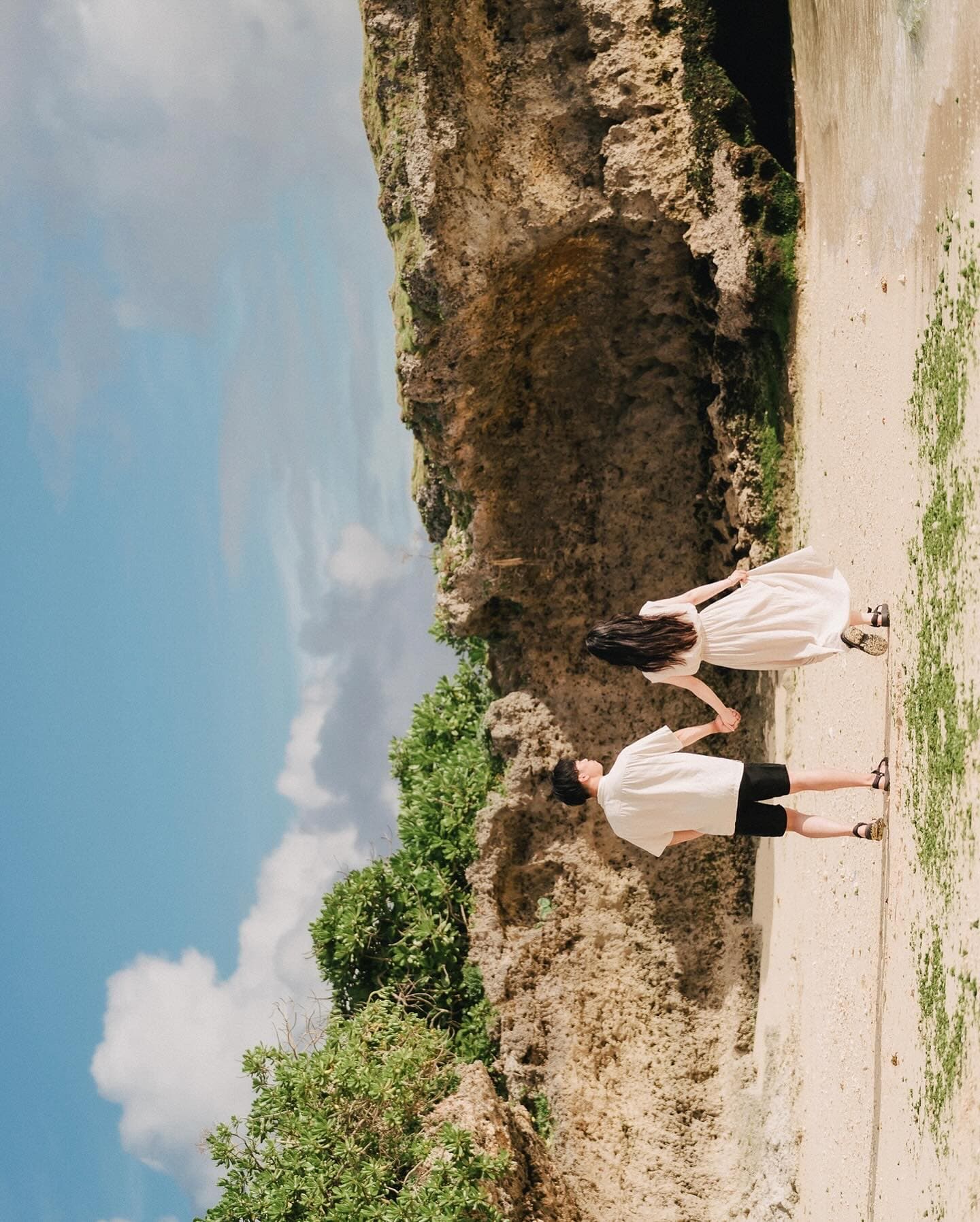 Couple walking hand in hand on a sandy path by rock cliffs in sunny Okinawa