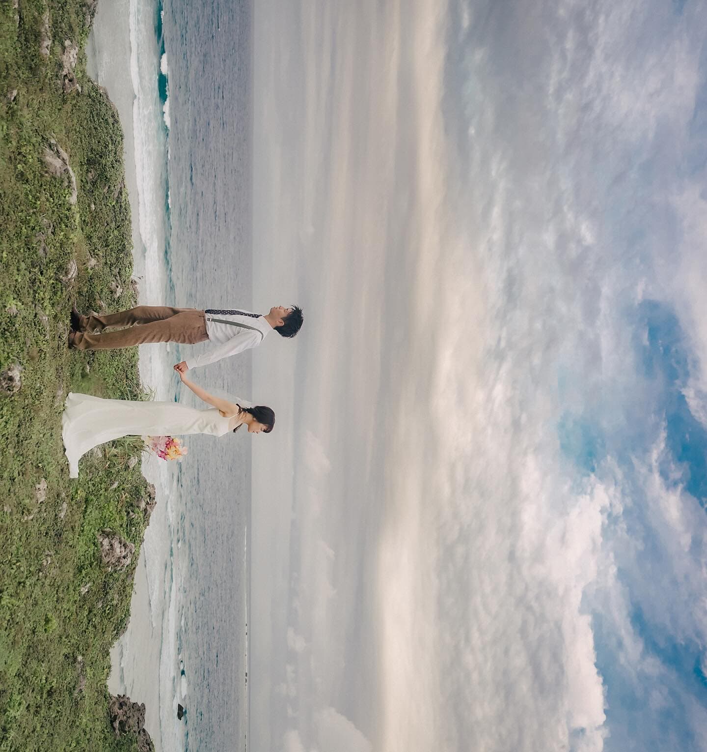 Couple walking hand in hand on a grassy cliff over the Miyakojima sea