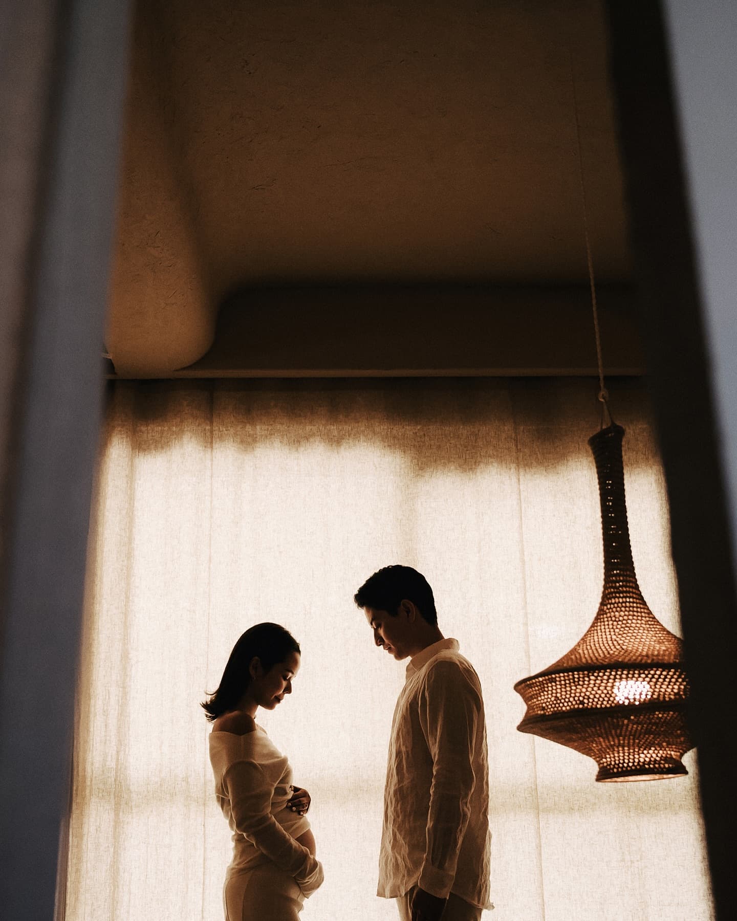 An expecting couple in silhouette before a backlit studio curtain